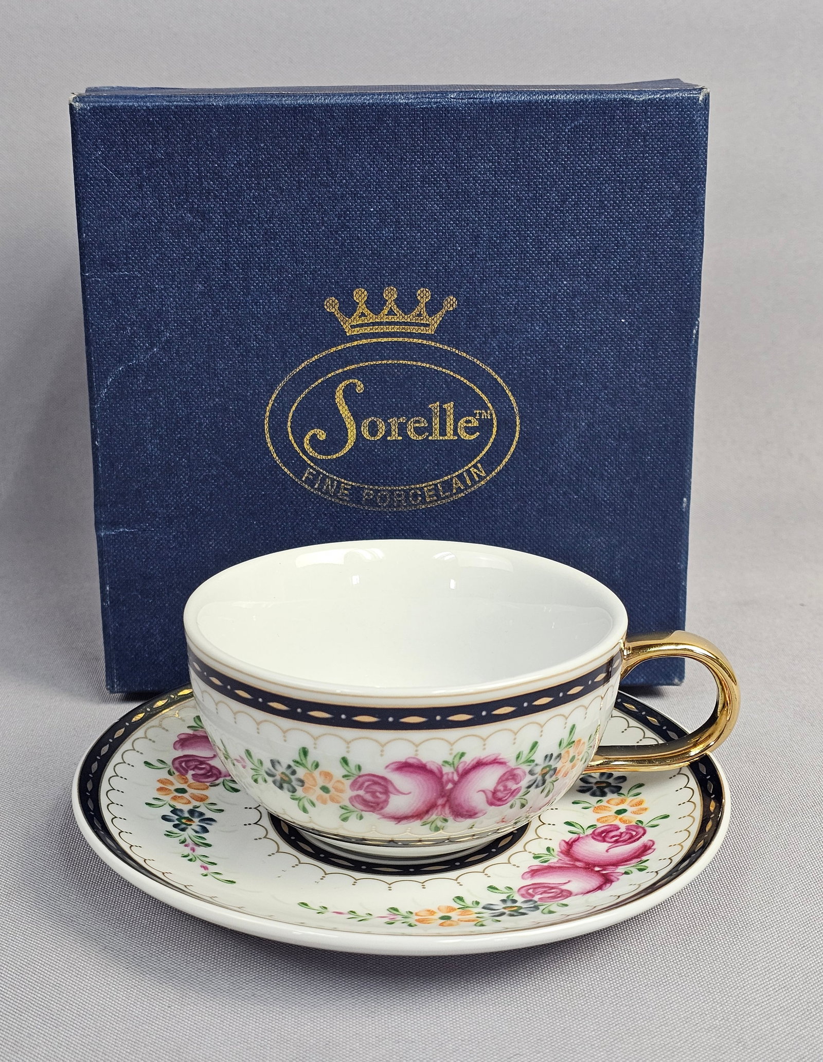 Sorelle Fine Porcelain Pink Rose Tea Cup & Saucer Set: A Pair of Sorelle Fine Porcelain items comprising a tea cup and matching saucer decorated with a pink rose pattern. Both pieces feature a white porcelain ground with floral sprays of pink roses, blue 