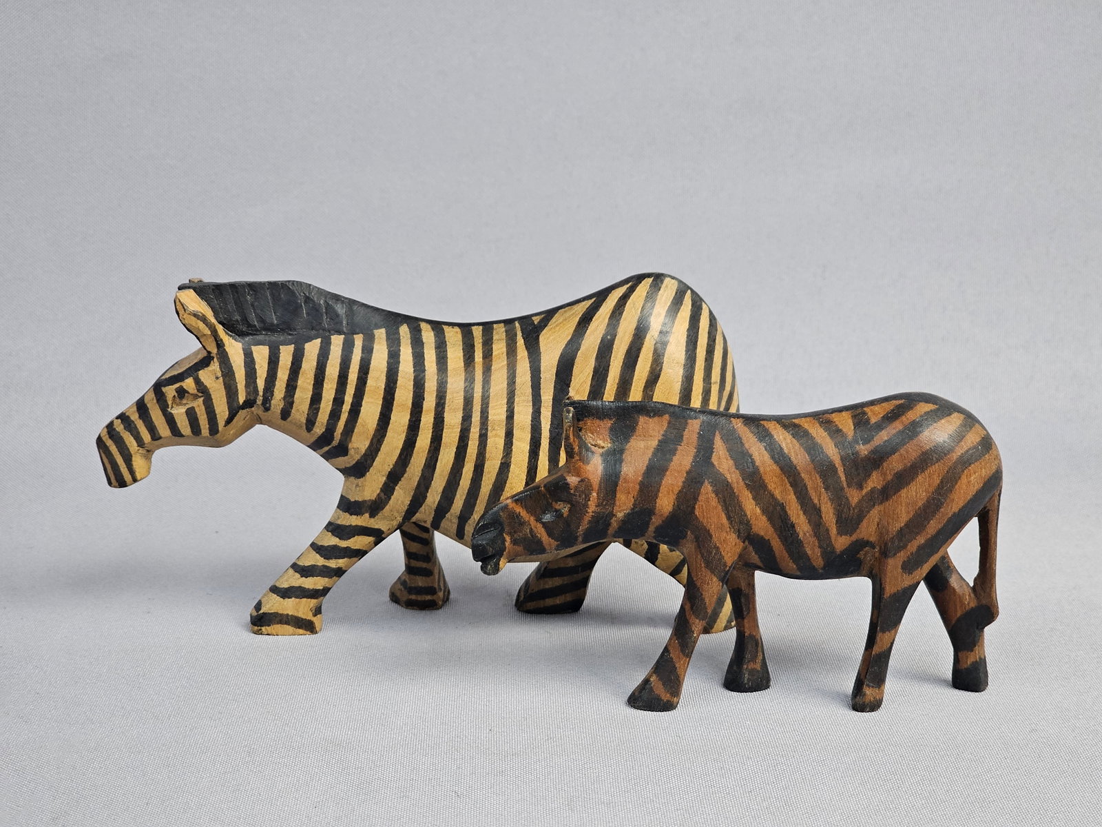 Pair of Hand-Carved and Painted Wooden Zebra Figurines: This lot consists of a pair of hand-carved and hand-painted wooden zebra figurines, which are in the style of Kenyan artisanal folk art. The pair includes one larger adult zebra and one smaller