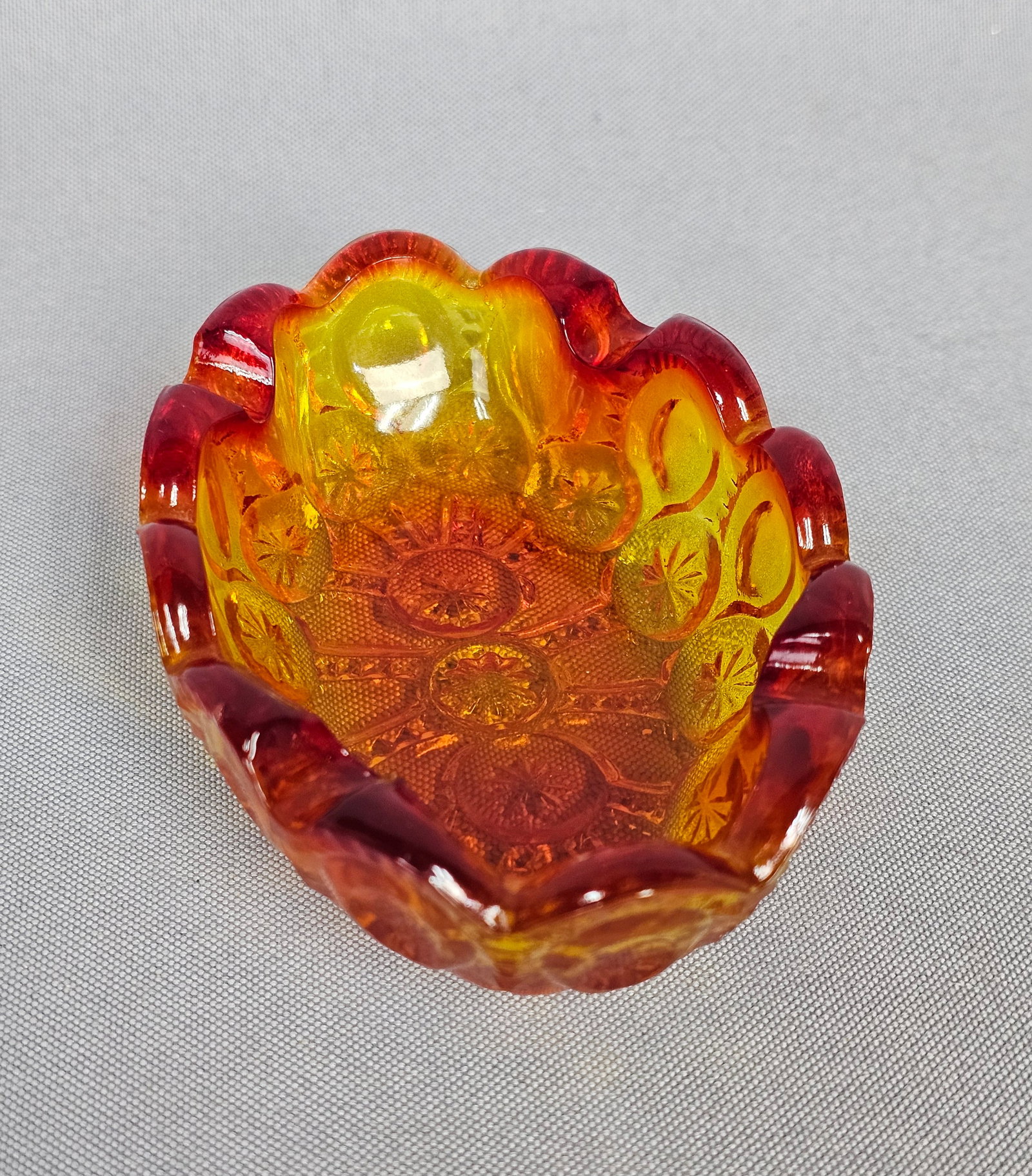 Small Amberina Moon & Star Pattern Oval Dish: This is a small, oval-shaped dish made of pressed glass, featuring the classic Moon and Star pattern. The pattern is distinguished by its repeating design of large circular punties (moons) and