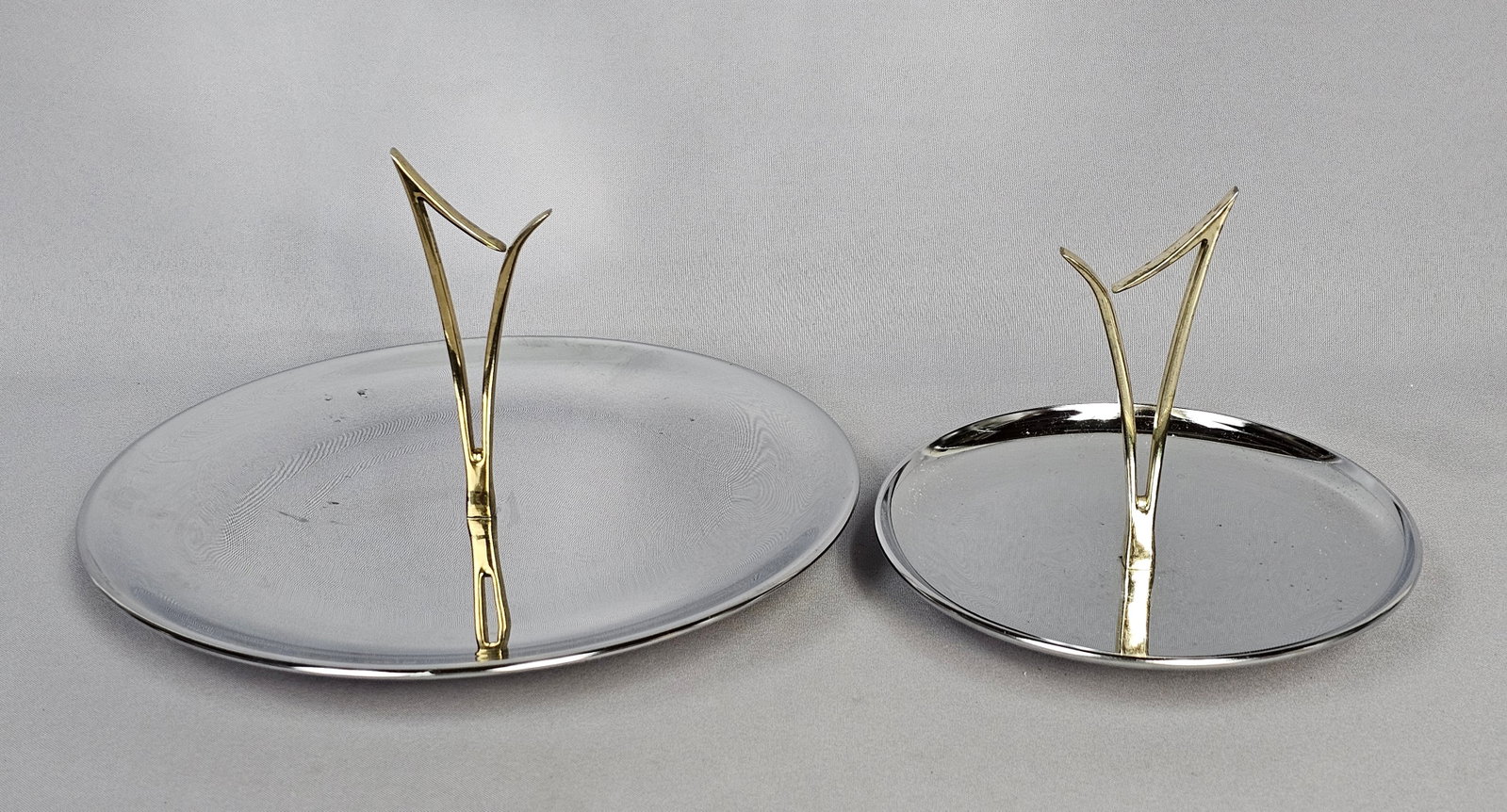 Mid-Century Modern Chrome & Gold-Tone Serving Trays: The items are characteristic of the 1950s and 1960s atomic style, featuring polished chrome-plated metal bodies and stylized abstract cast gold-tone handles. Each central handle is secured to its base