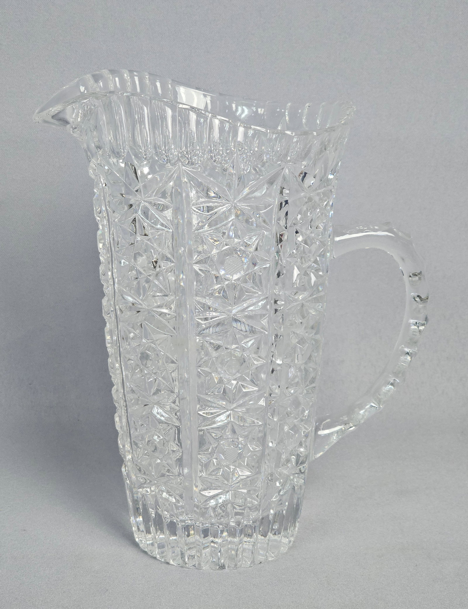American Brilliant Period Cut Glass Water Pitcher: This is a tall, handled water pitcher crafted from heavy lead crystal, characteristic of the American Brilliant Period. The exterior body features deep mitre cuts arranged in vertical panels. No