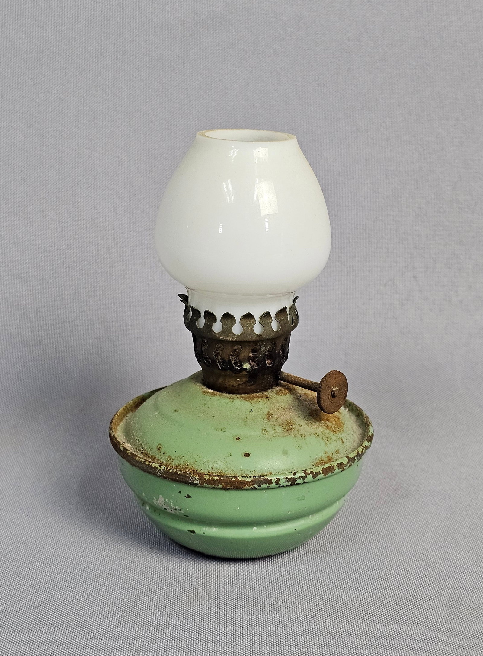 Miniature Kelly Style Metal Oil Lamp: This object is a miniature weighted oil lamp, often referred to as a Kelly lamp or pixie lamp. It features a self-righting design with a rounded, weighted metal base finished in green paint. The lamp