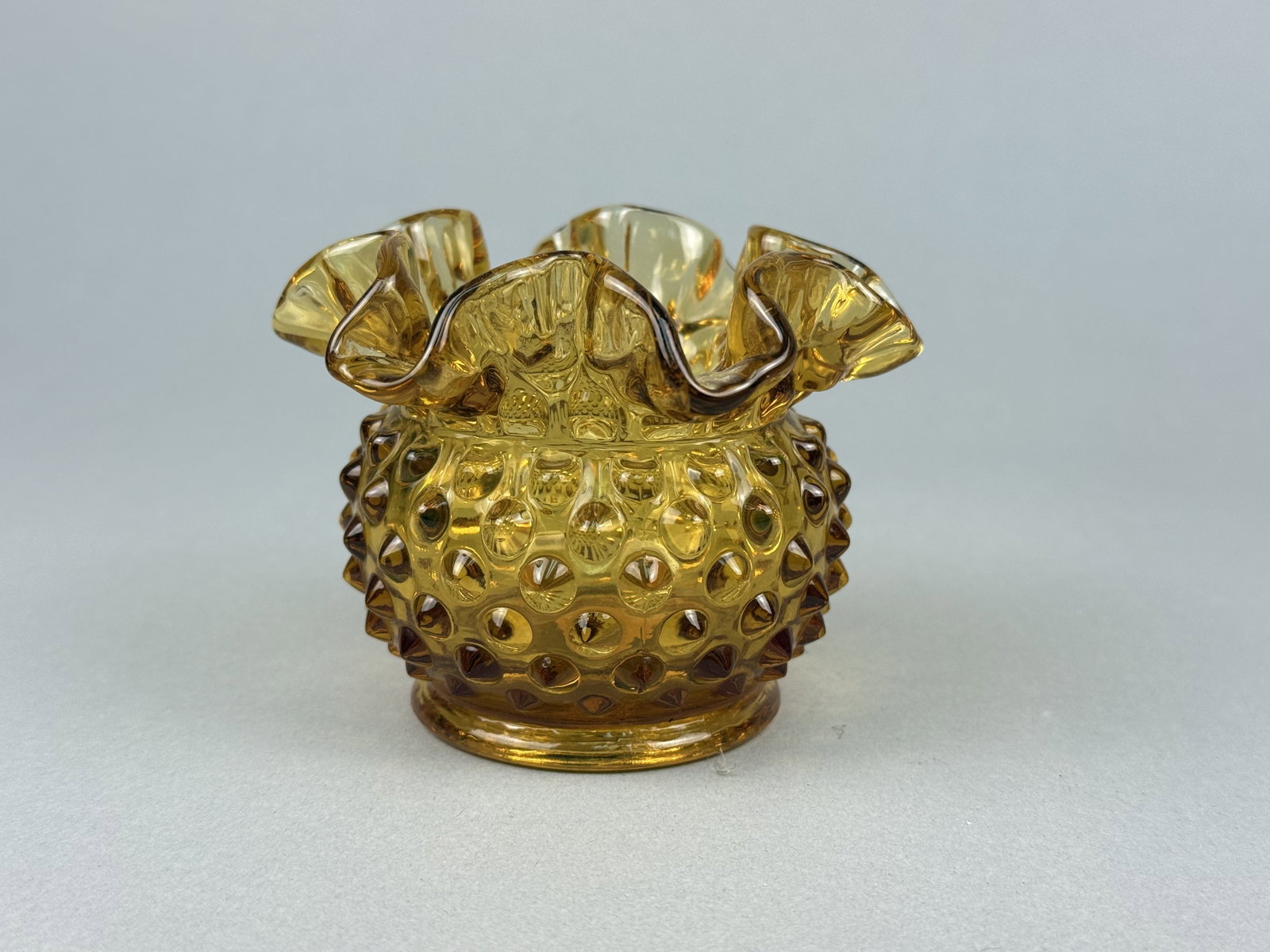 Fenton Amber Hobnail Glass Ruffled Rose Bowl: This is a small rose bowl or miniature vase produced by Fenton Art Glass. The piece is crafted from pressed amber glass and features the company's signature dense hobnail pattern across the bulbous