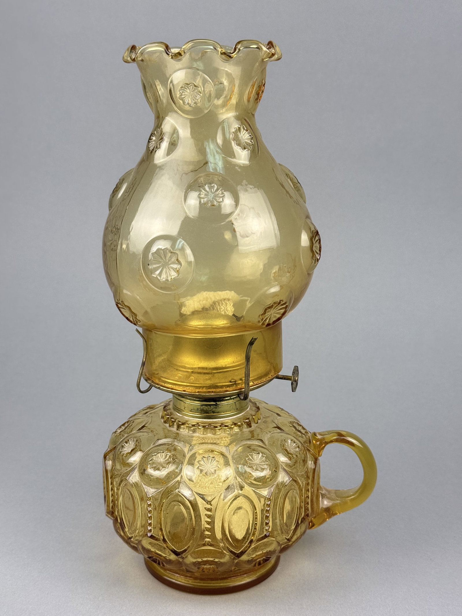 Vintage Amber Moon and Star Pattern Glass Oil Lamp: This lot consists of an amber pressed glass oil lamp in the Moon and Star pattern. While no maker's mark is present, the color and pattern are characteristic of mid-20th-century reproductions