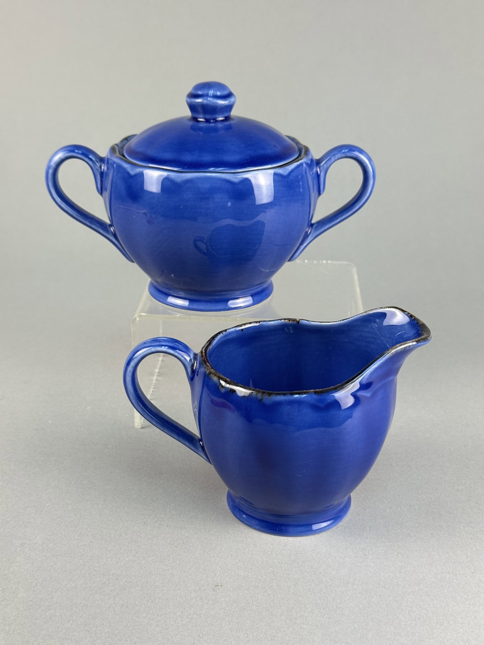 W.H. Grindley Cobalt Blue Glazed Earthenware Sugar Bowl & Creamer: This two-piece earthenware set includes a matching lidded sugar bowl and creamer, both finished in a vibrant cobalt blue glaze. The underside of each piece features an impressed manufacturer's mark
