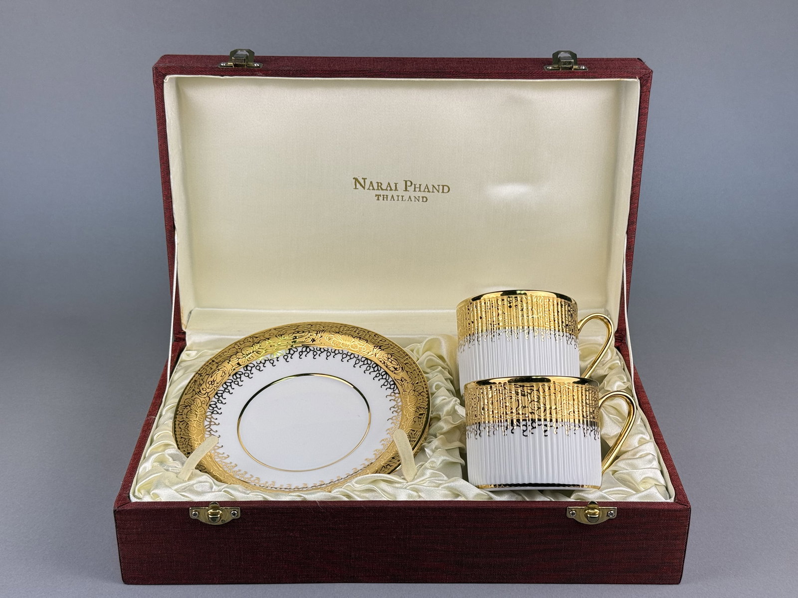 Royal Porcelain Hand Painted Gilded Cups & Saucers for Narai Phand: This is a boxed set of two hand painted and gilded porcelain cups and saucers, manufactured by Royal Porcelain for Narai Phand in Thailand. The base of each cup is marked with blue and green stamps st