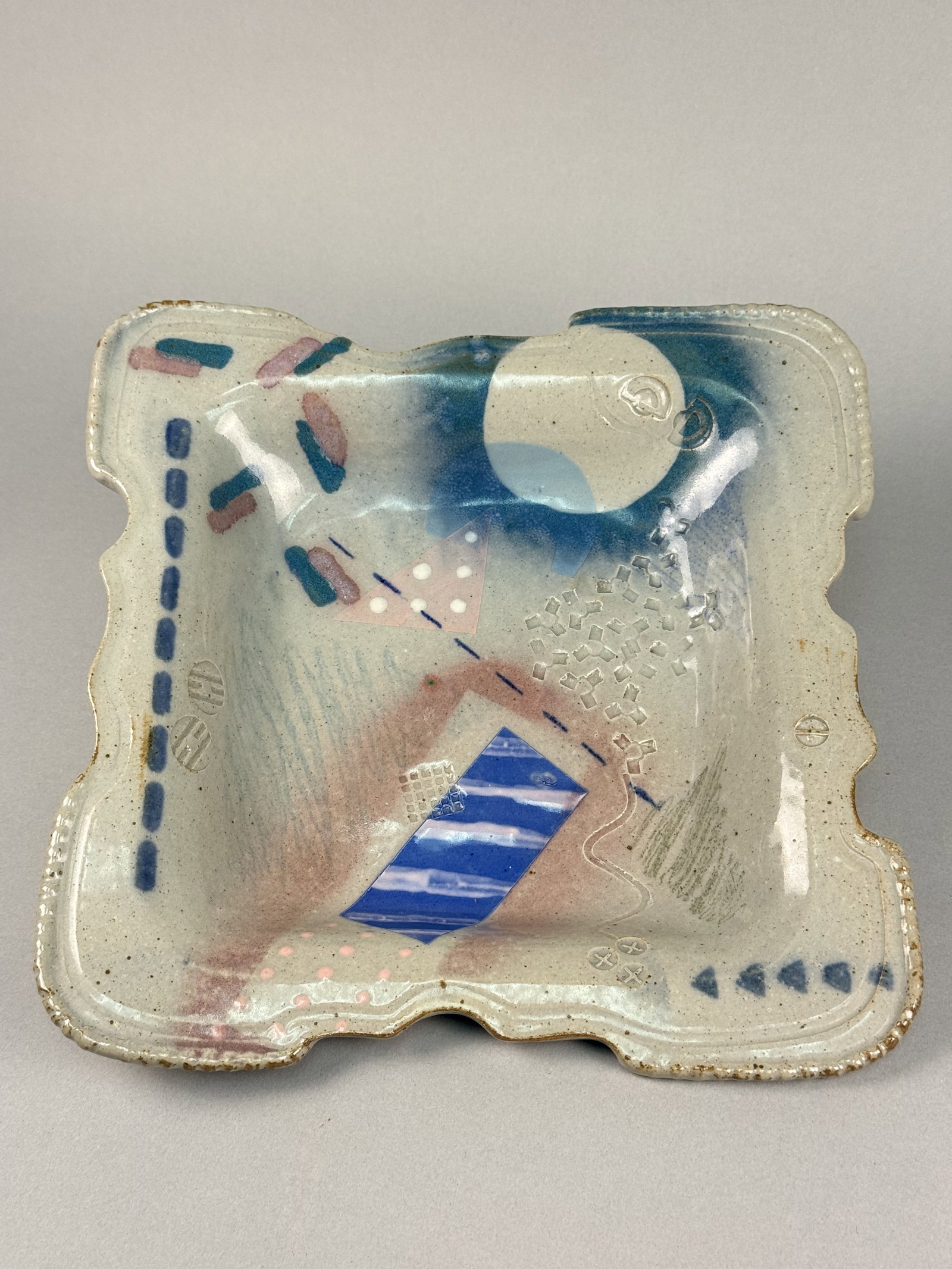 Signed Postmodern Memphis Style Studio Ceramic Square Bowl: The stoneware vessel is square in form with an irregular, undulating scalloped rim and slightly raised corners. The unglazed underside shows a coarse, light tan speckled clay body and is incised with 