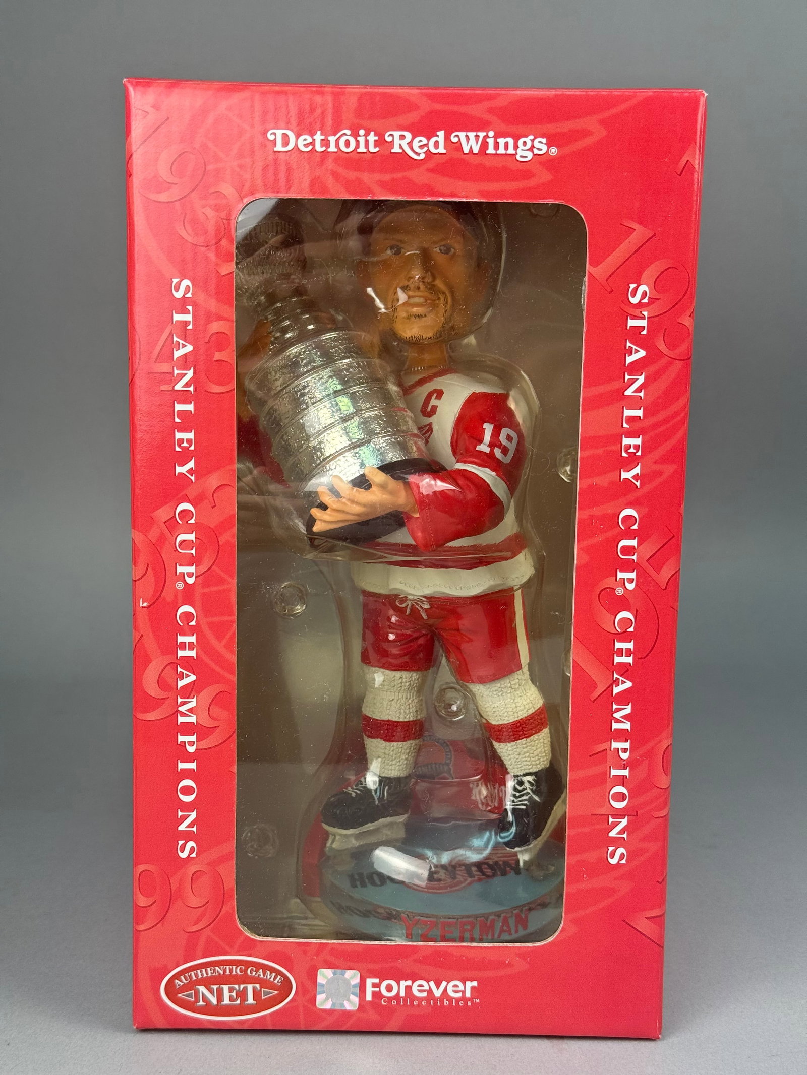 Steve Yzerman Detroit Red Wings Bobblehead 2002 Stanley Cup Champions: The figurine depicts Captain Steve Yzerman in a home white jersey featuring his number 19 and a captain's C patch, while holding the Stanley Cup trophy. A key feature of this collectible is the