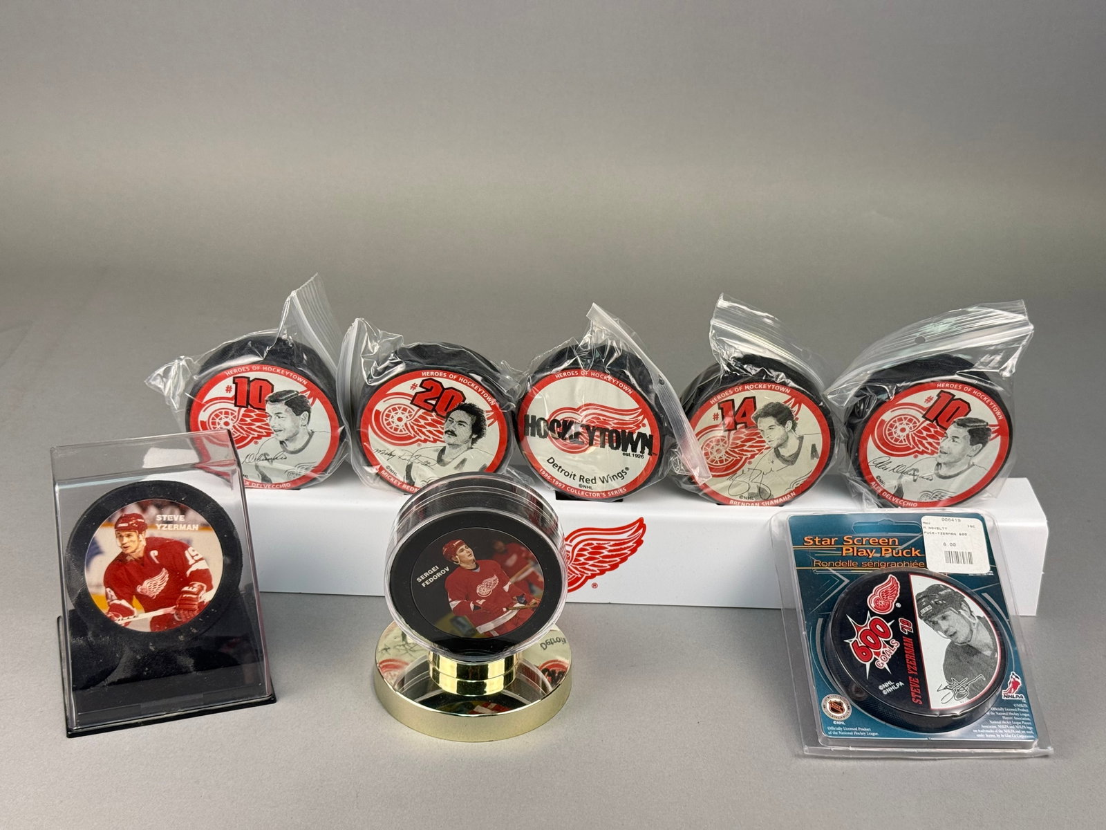 Eight Detroit Red Wings Souvenir Hockey Pucks & Display Accessories: This collection consists of eight Detroit Red Wings souvenir hockey pucks featuring various players and team history, along with three display accessories. These pucks include printed facsimile