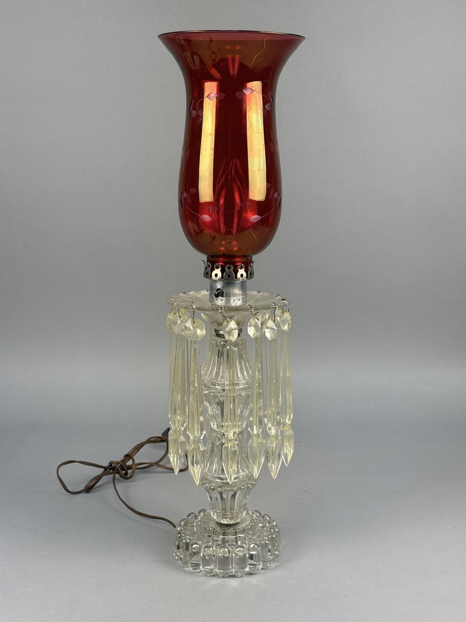 Vintage Ruby Red Etched Glass Hurricane Table Lamp: This vintage electric hurricane-style table lamp features a ruby red glass shade and a clear pressed glass base. The shade is designed in a flared chimney form and is decorated with wheel-etched or