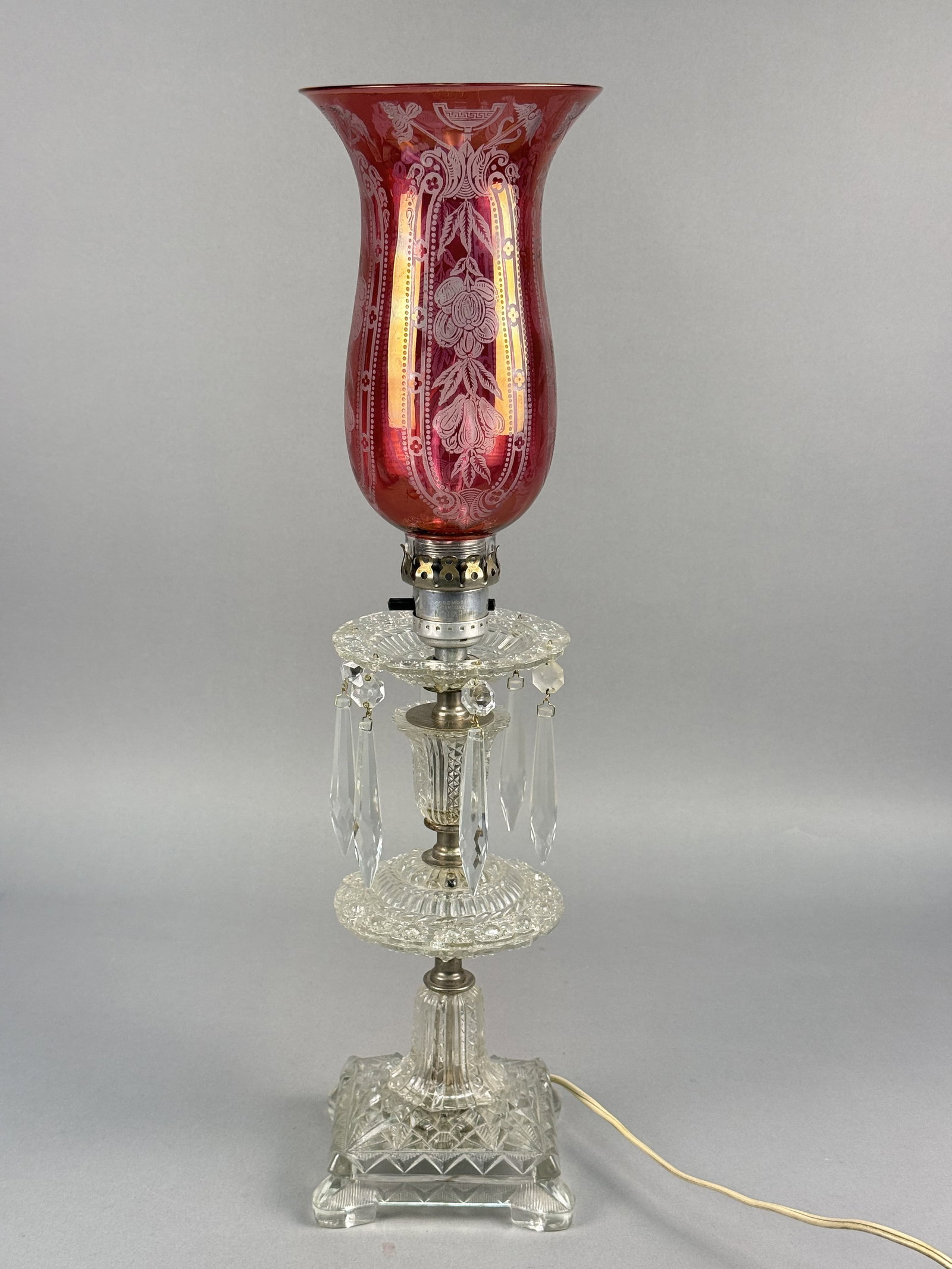 Cranberry Etched Glass Hurricane Table Lamp: This electric table lamp is designed in the Victorian Revival style, commonly referred to as a hurricane or mantle lamp. The lamp is fitted with a vintage tan two-strand cord and a white molded