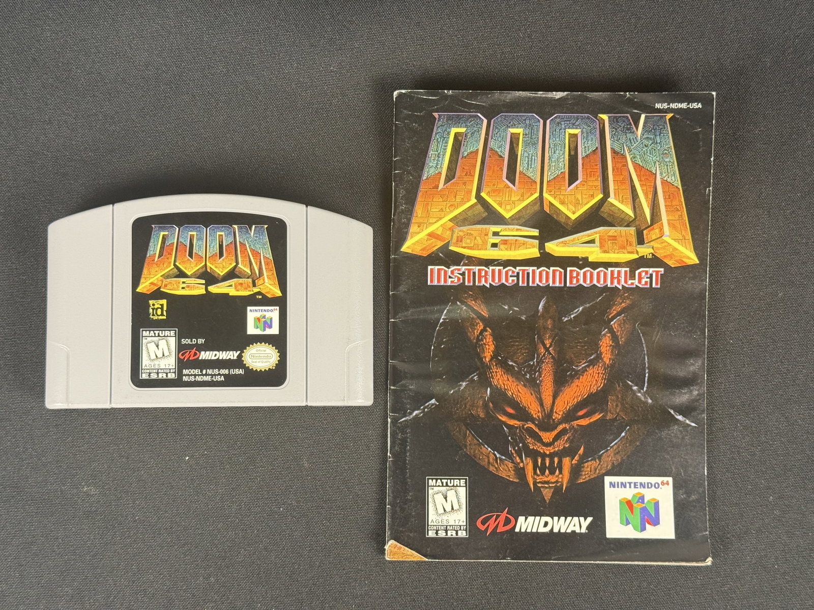 Nintendo 64 Doom 64 Game Cartridge & Instruction Booklet: l. The front label features the game title logo, logos for Midway and id Software, an ESRB Mature rating, and the code NUS-NDME-USA. The reverse of the cartridge shell is embossed with the Nintendo