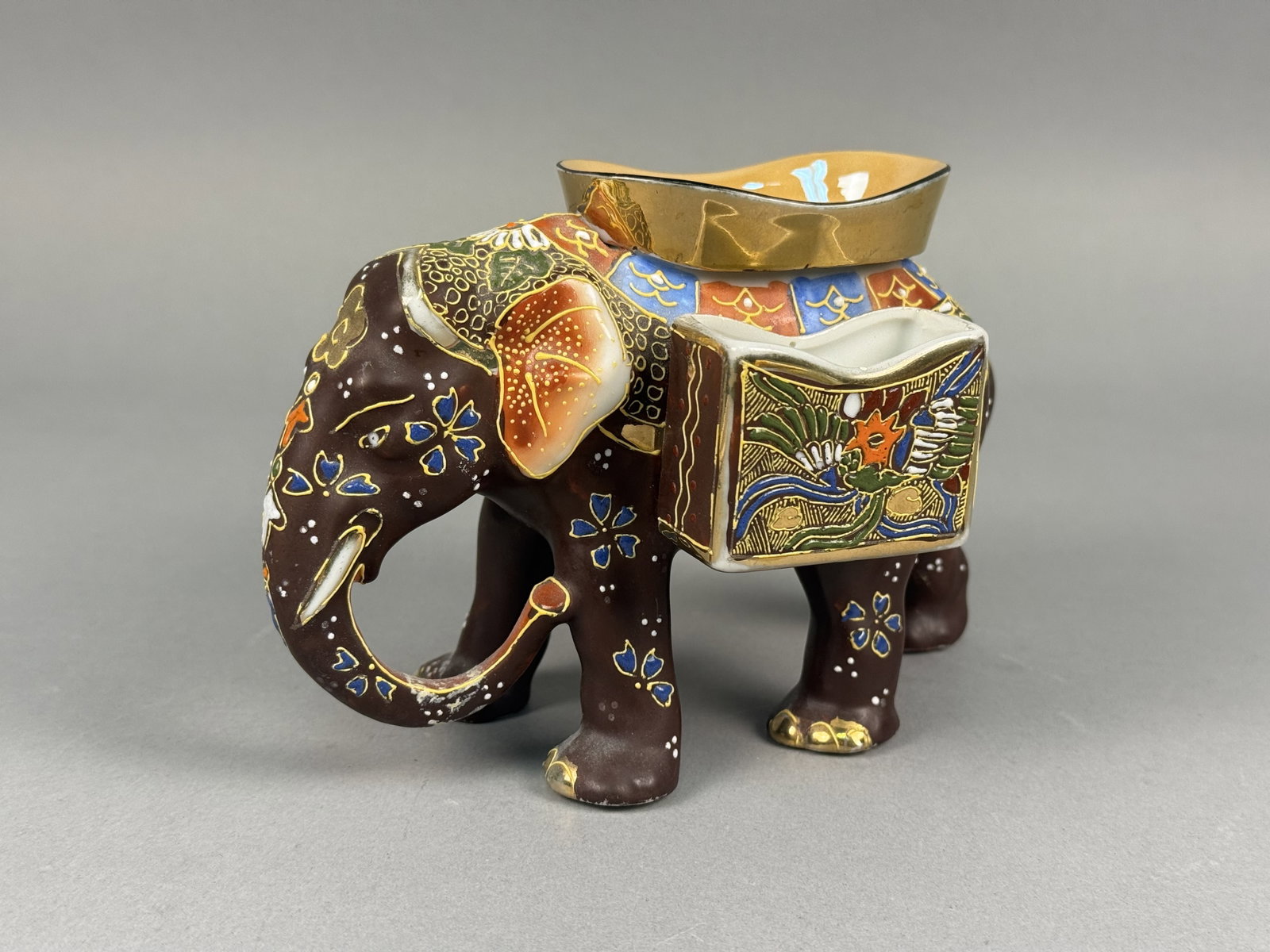 Japanese Moriage Porcelain Elephant Ashtray & Matchbook Holder: The figurine is finished in a matte dark brown glaze and features elaborate moriage decoration with raised enamel in shades of blue, red, green, yellow, and white. The underside of one foot bears a ci