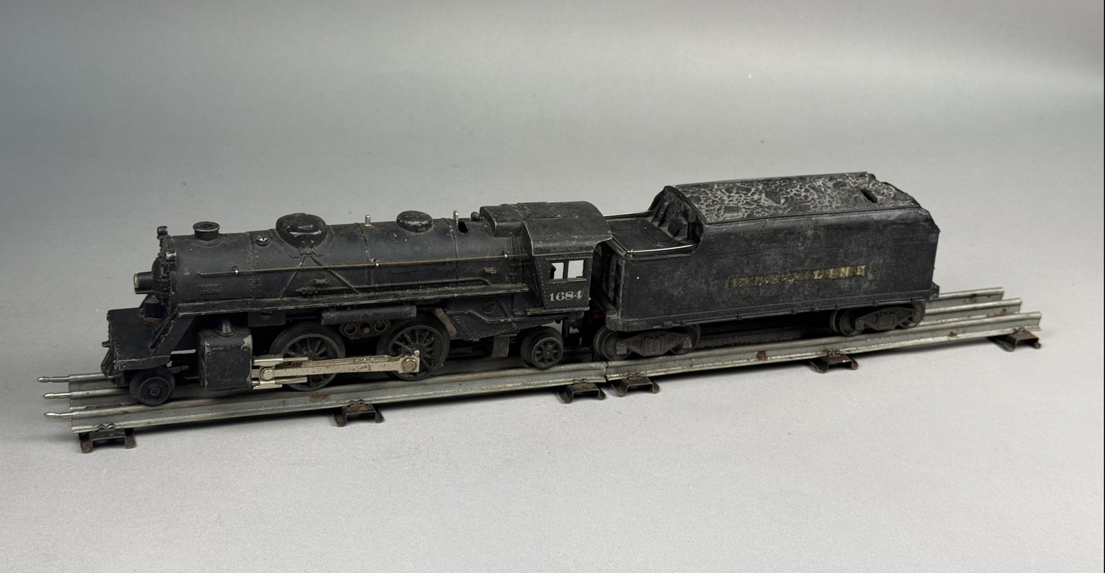Lionel O-Gauge No. 1684 Steam Locomotive & No. 2466WX Whistling Tender: This lot features an O-gauge electric toy train steam locomotive and whistling tender manufactured by The Lionel Corporation. The locomotive is a No. 1684 2-4-2 steam engine constructed of die-cast me