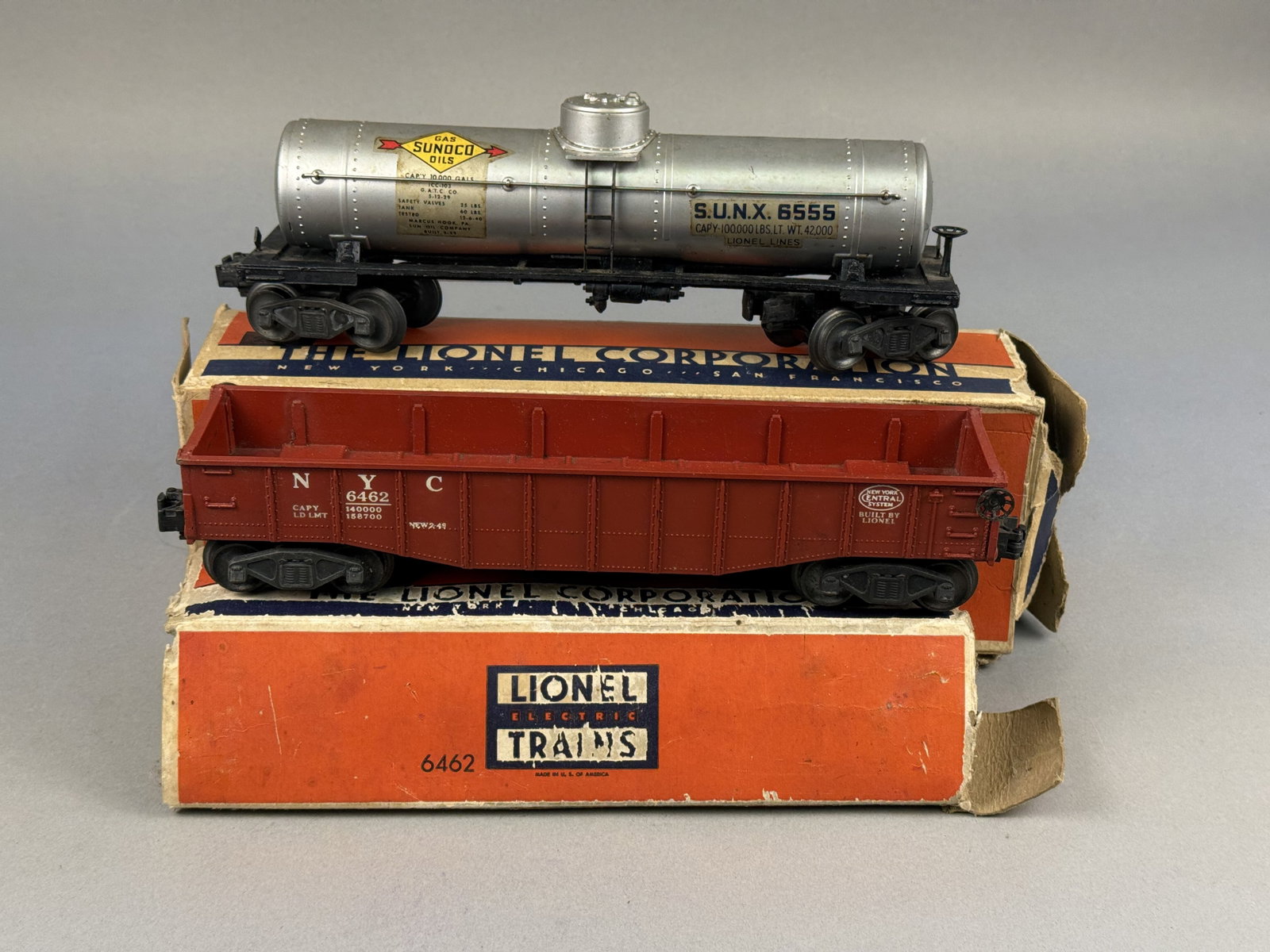 Two Lionel Postwar O-Gauge Freight Cars No. 6555 Sunoco Tank Car & No. 6462 NYC Gondola: The first item is a No. 6555 Sunoco tank car, constructed with a painted silver plastic tank mounted on a black die-cast metal frame. The frame is embossed on the underside with No. 2955, Made in U.S.