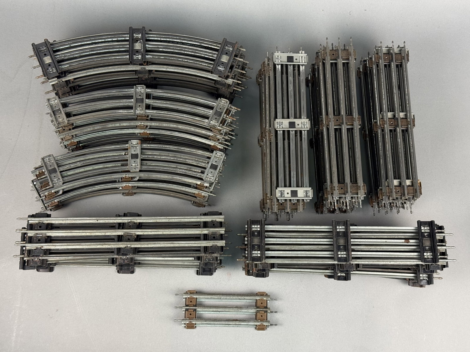 Lionel O Gauge & O-27 Gauge Three-Rail Model Train Track: This lot features a collection of vintage three-rail tubular model train track, primarily O gauge and O-27 gauge. The track sections are constructed with tinplate steel rails and a combination of