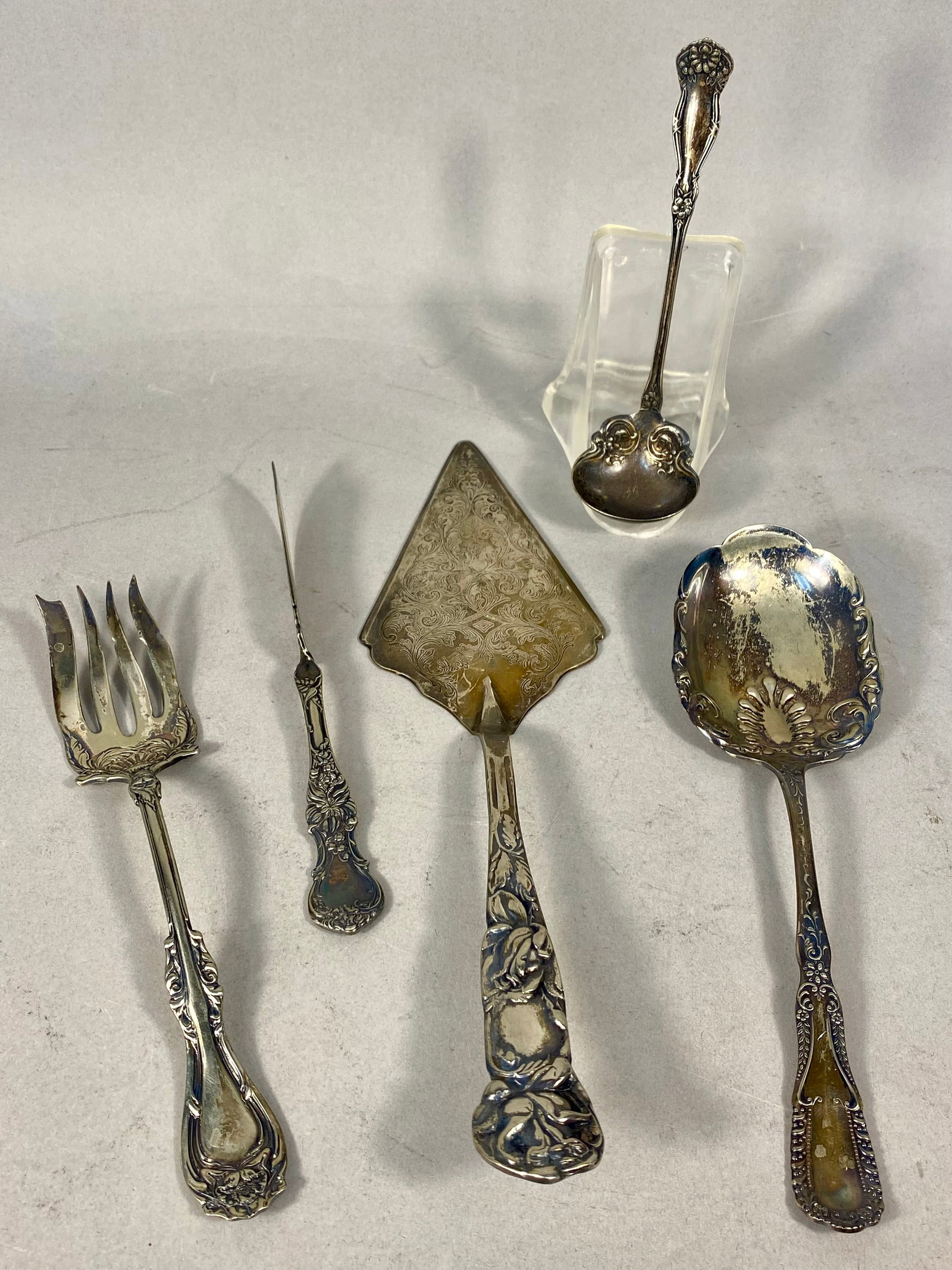 Five Silver-Plated Serving Pieces Including Cartier, Rogers, and Wallace: This collection consists of five assorted silver-plated serving pieces from multiple makers. The first item is a large cake or pie server marked Cartier Italy on the handle, featuring an engraved