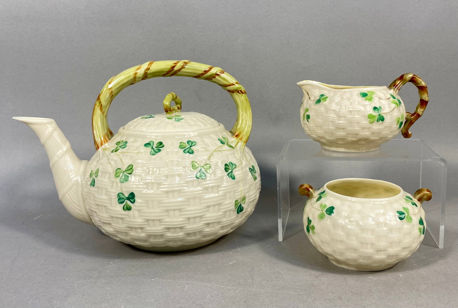 Three Irish Belleek Shamrock Pattern Porcelain Tea Set Pieces: This lot features a three-piece Parian porcelain tea set from Belleek Pottery of Ireland, decorated in the classic Shamrock pattern. The set includes a lidded teapot, an open creamer, and an open suga
