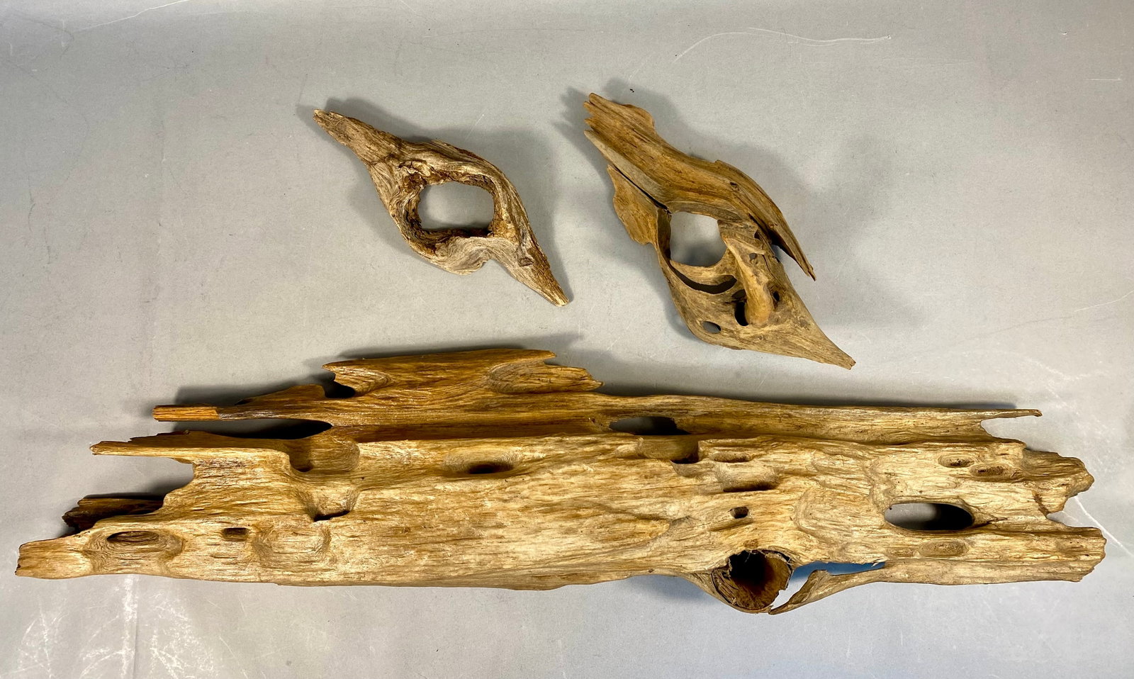 Natural Driftwood Wall Hangings: A group of three natural driftwood pieces affixed with hangers for wall decor. Including a large piece and two smaller accent fragments. The items are crafted from natural wood, likely cedar or