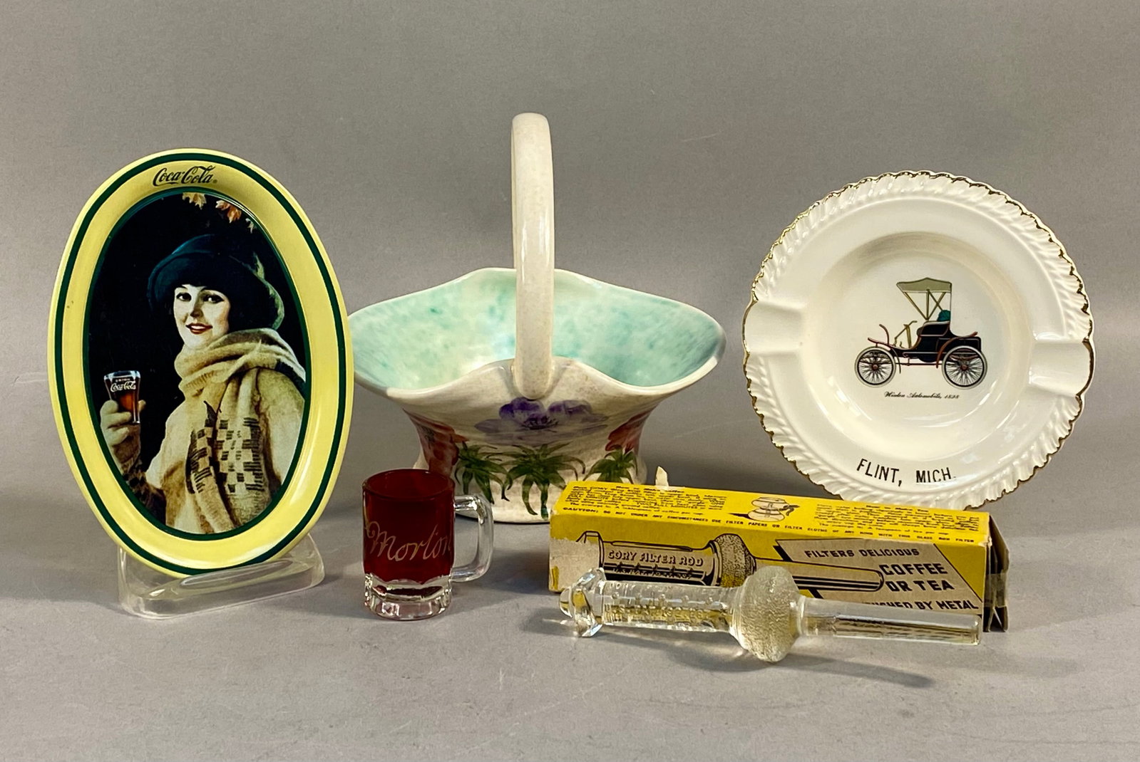 Vintage Advertising and Souvenir Collectibles: A collection of assorted vintage items including an oval metal Coca-Cola advertising tray, a hand-painted ceramic basket, a ceramic souvenir ashtray, a miniature ruby glass mug, and a boxed glass