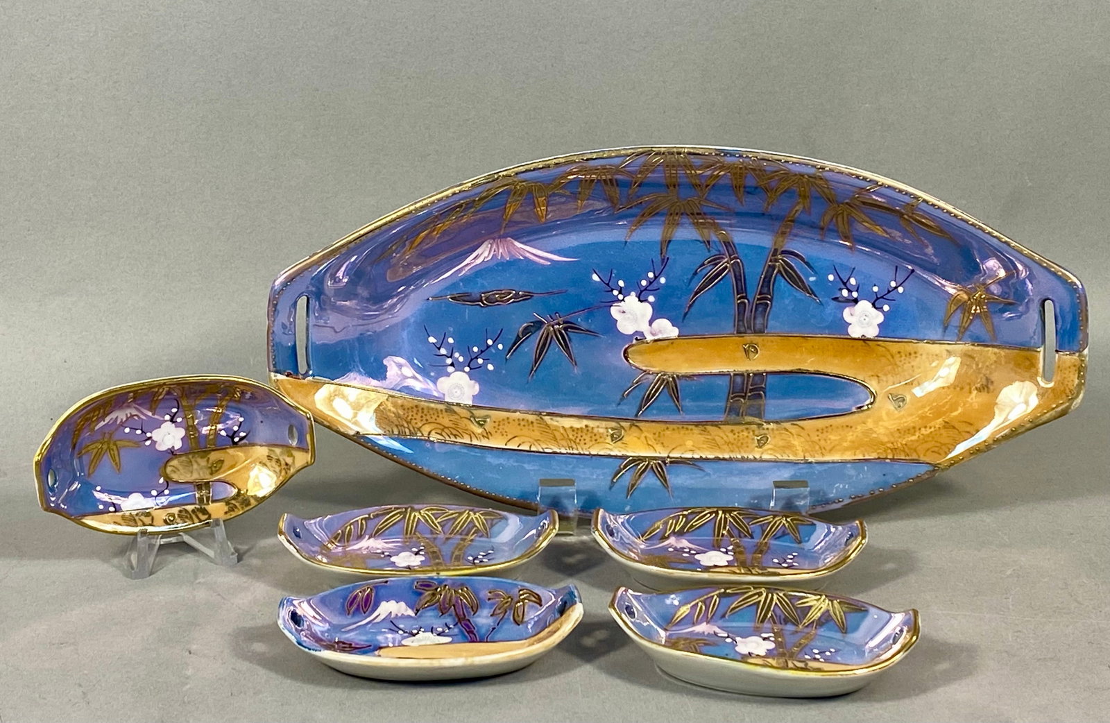 Six-Piece Japanese Hand-Painted Porcelain Condiment Set: A six-piece Japanese hand-painted porcelain nut or condiment set. The set comprises one large oval tray with integrated cutout handles and five matching small individual dishes. Each piece is
