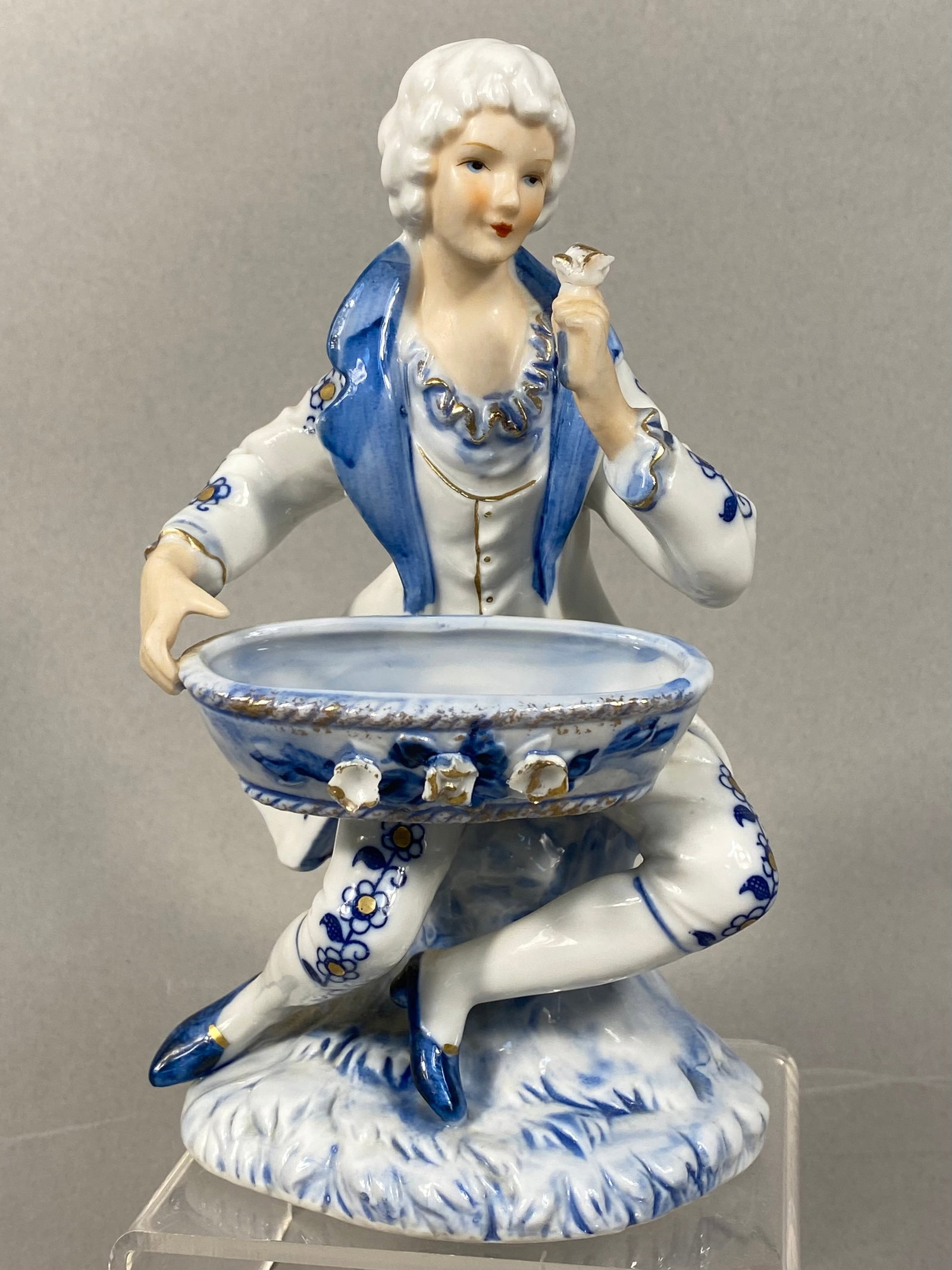 Porcelain Figural Dish in the Style of Meissen Blue Onion: This porcelain figurine serves as a figural sweetmeat dish or salt cellar, featuring a seated male courtier in 18th-century attire. The figure wears a powdered wig, a floral-patterned frock coat, and