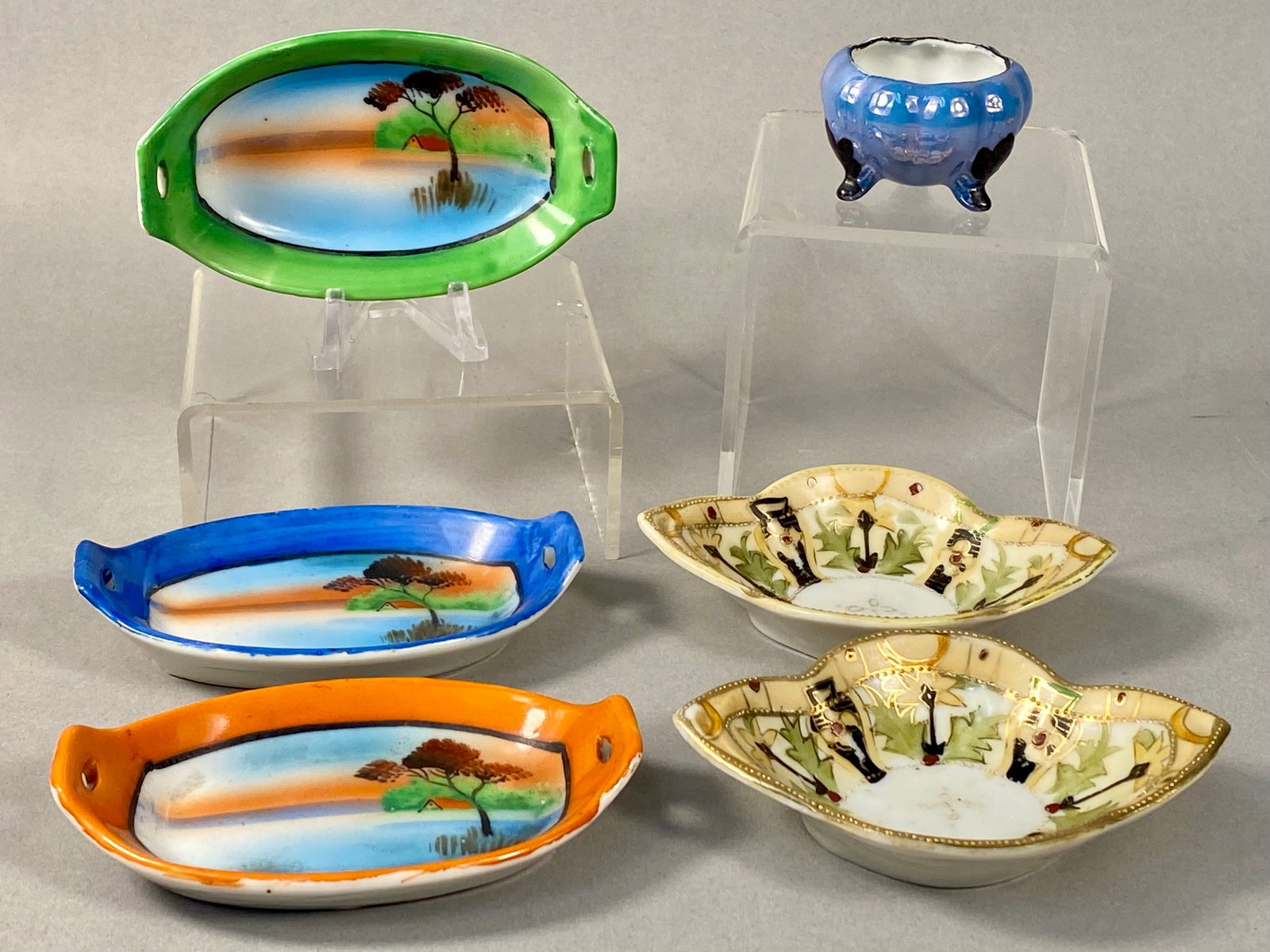 Six Japanese Miniature Lusterware Porcelain Dishes: An assortment of Japanese six miniature porcelain items manufactured for the export market. One group consists of oval trays with twin handles, hand-painted with a sunset landscape scene depicting a t