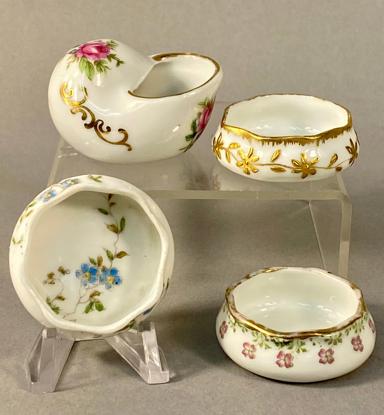 Four Limoges & Imported Miniature Porcelain Dishes: Four miniature porcelain open salts featuring hand-painted floral decorations and gilded accents. One piece is modeled as a nautilus shell and features hand-painted pink roses with green foliage and r