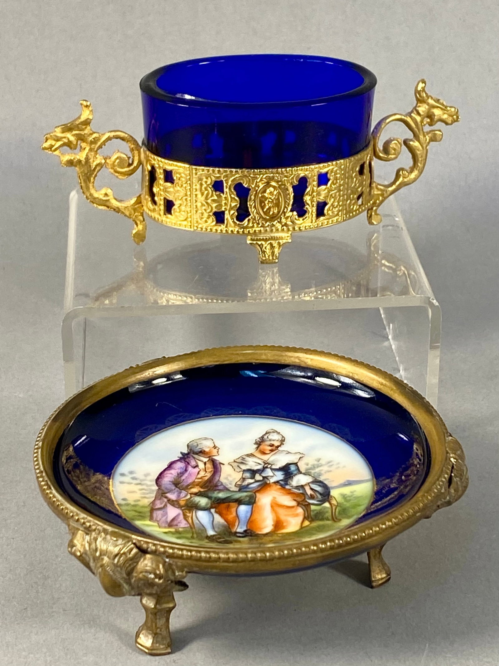Two Czechoslovakian Cobalt Blue & Gilt Metal Table Articles: This lot consists of two decorative items featuring cobalt blue glass and gilt metal mounts. The first item is a small footed dish with a cobalt blue body and a central hand-painted porcelain