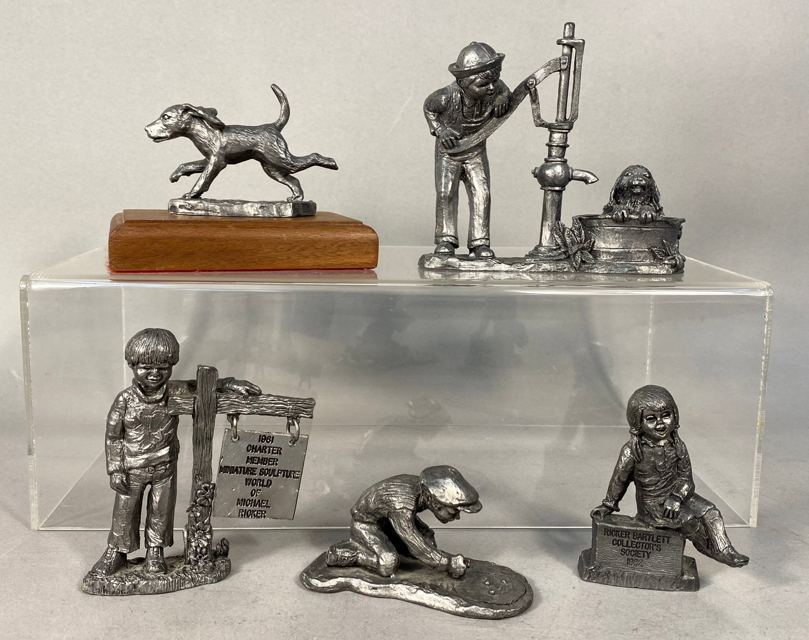 A Collection of Five Michael Ricker Pewter Figurines: This lot consists of five cast pewter miniature figurines designed by Michael Ricker for Ricker Bartlett. The collection features nostalgic Americana themes including a running hound dog mounted on a