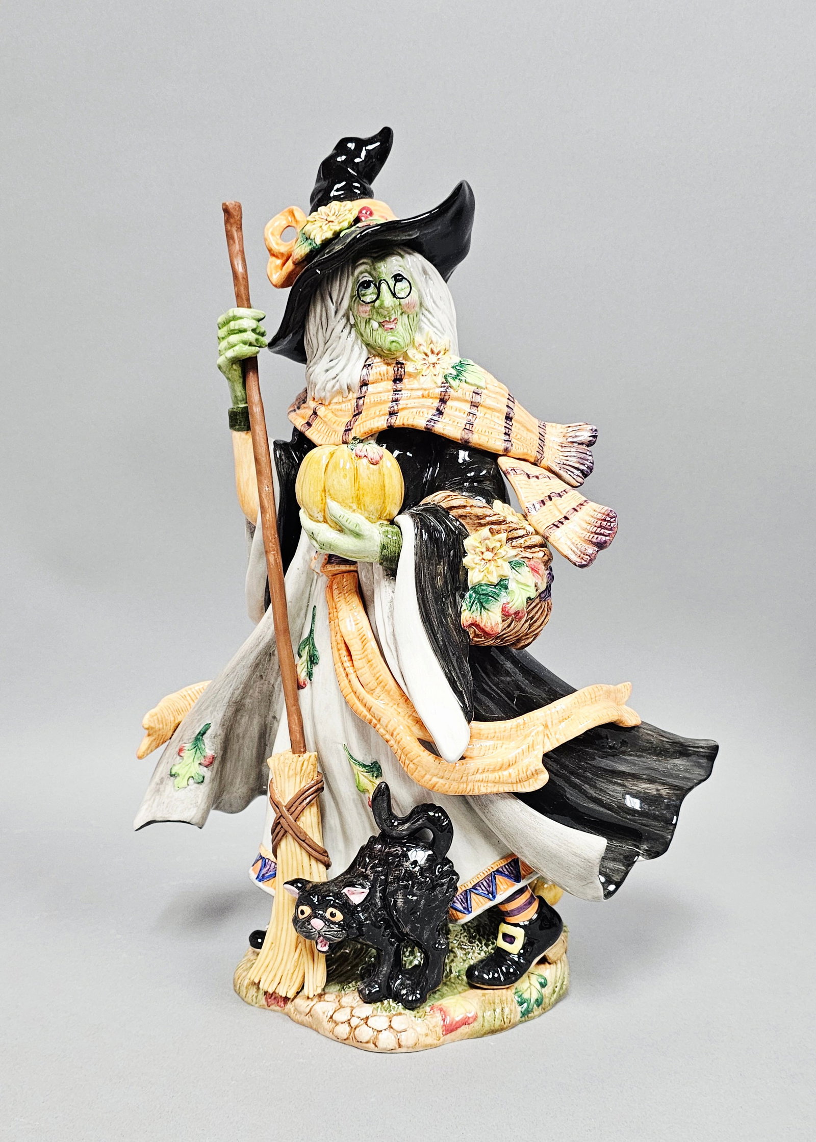 Fitz and Floyd Halloween Harvest Witch Figurine: This hand-painted glazed ceramic figurine is part of the Fitz and Floyd Classics Halloween Harvest collection. The piece depicts a festive witch characterized by a green complexion, white hair, and sm