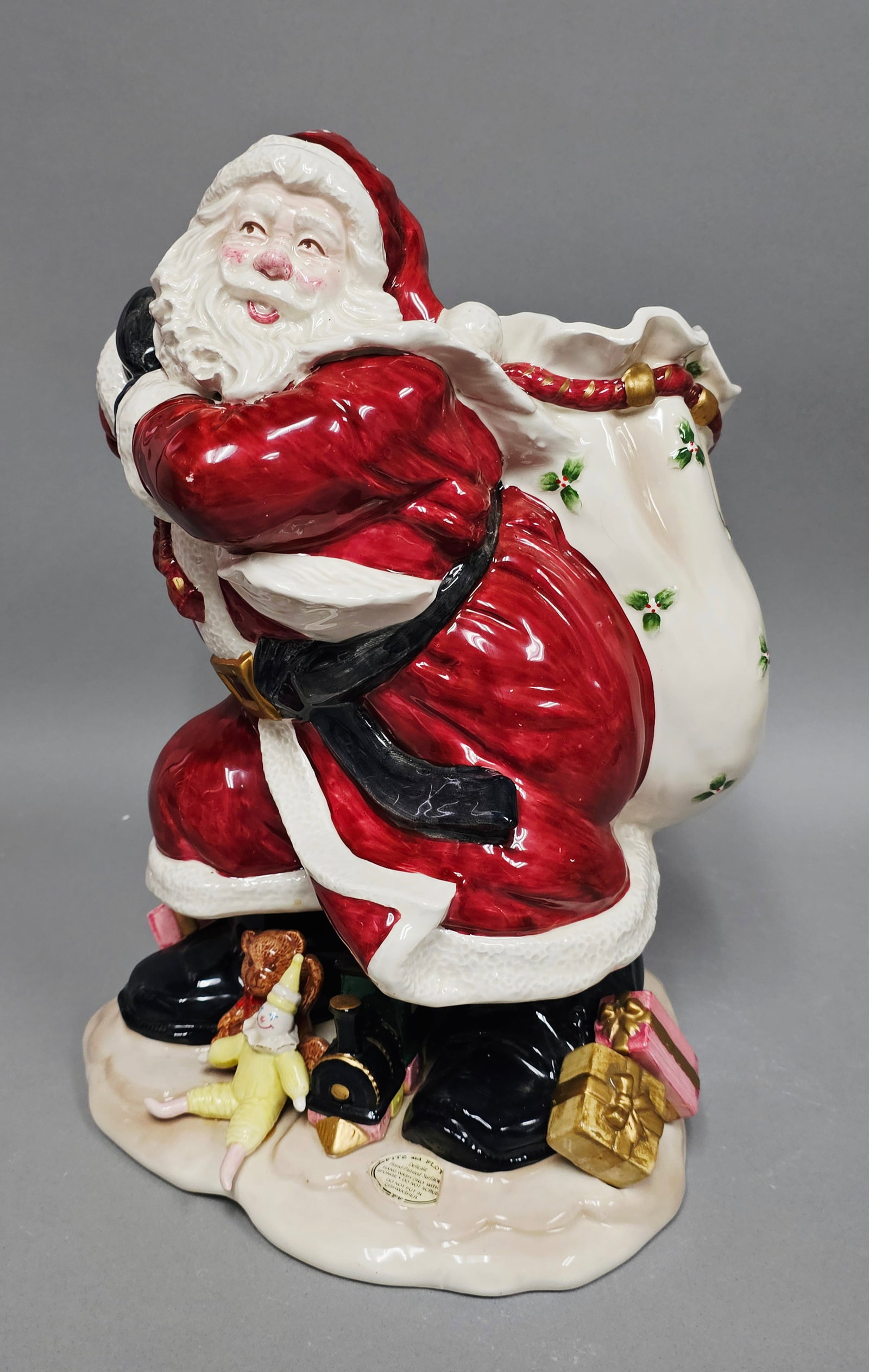 Fitz and Floyd 1987 Santa with Open Bag Vase: A large Fitz and Floyd hand-painted glazed ceramic vase modeled as a jovial Santa Claus. The figure is depicted in a dynamic leaning pose, supporting a large ivory-toned sack on his back decorated