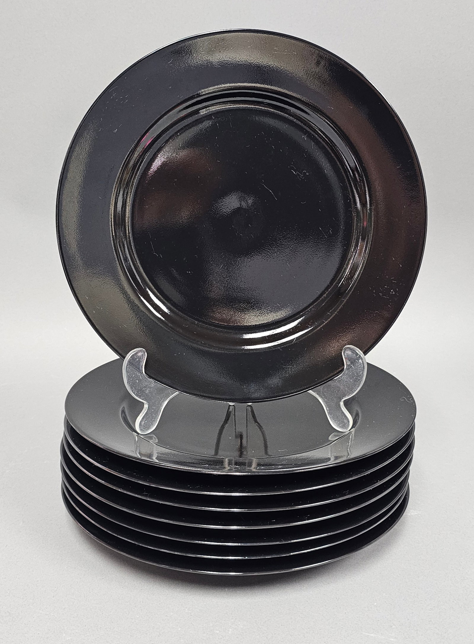Eight Fitz and Floyd Glazed Ceramic Plates: A set of eight glazed ceramic dinner or service plates by Fitz and Floyd. The plates feature a wide, flat rim and a circular recessed center, finished in a uniform, high-gloss solid black glaze. The