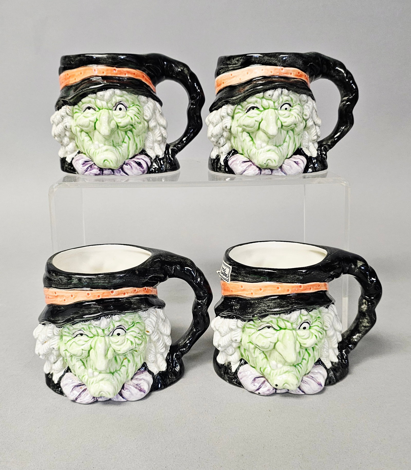 Four Fitz and Floyd Figural Witch Mugs: A set of four vintage ceramic figural mugs manufactured by Fitz and Floyd. Each mug is molded in the form of a green-skinned witch's head featuring a wrinkled face and a wink. The underside of each