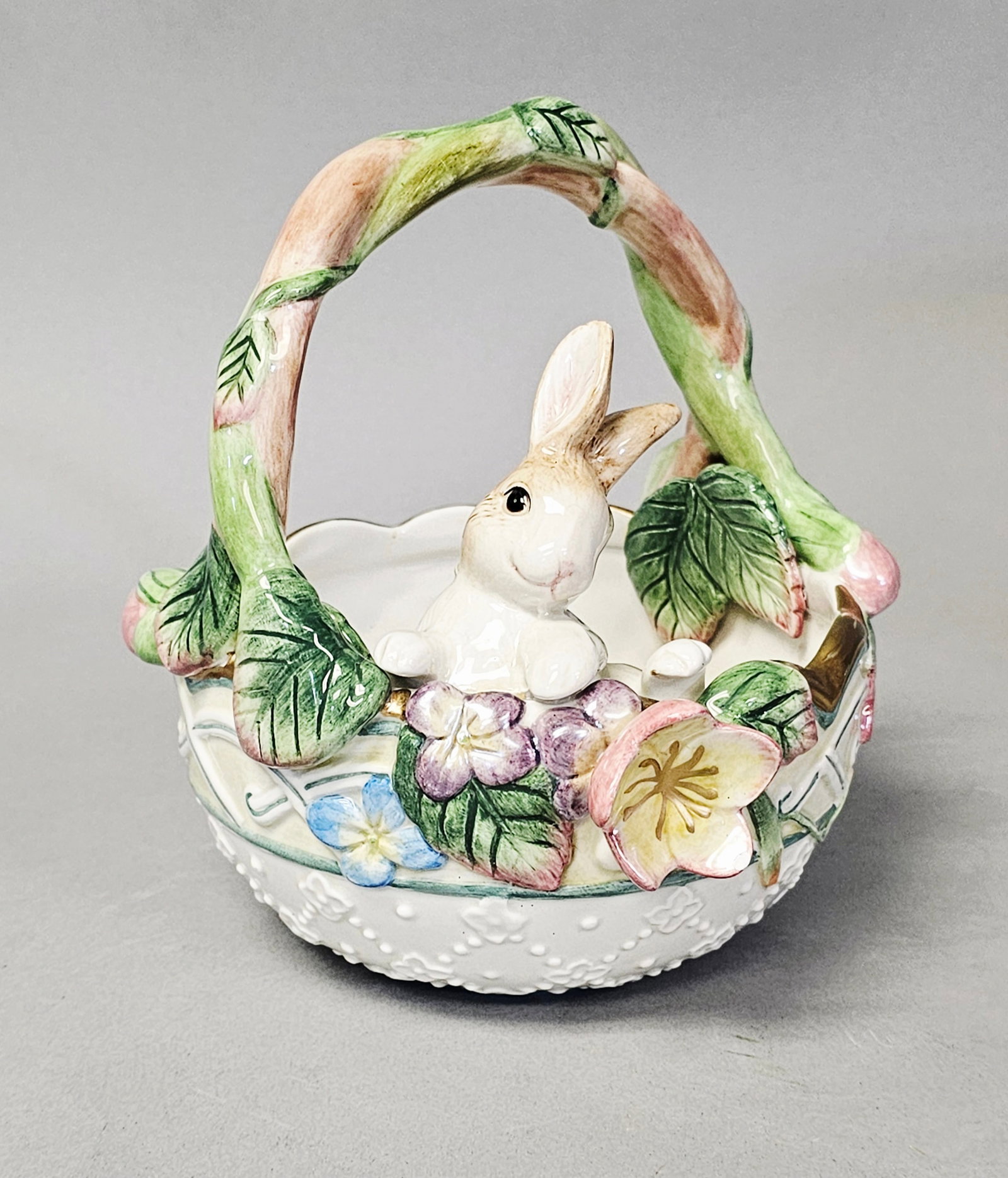 Fitz and Floyd Rabbit & Floral Decorative Basket: A handcrafted glazed ceramic decorative basket from the Fitz and Floyd Halcyon collection. The round basket features a high, arched handle modeled as a twisting green vine with leaf accents. The base
