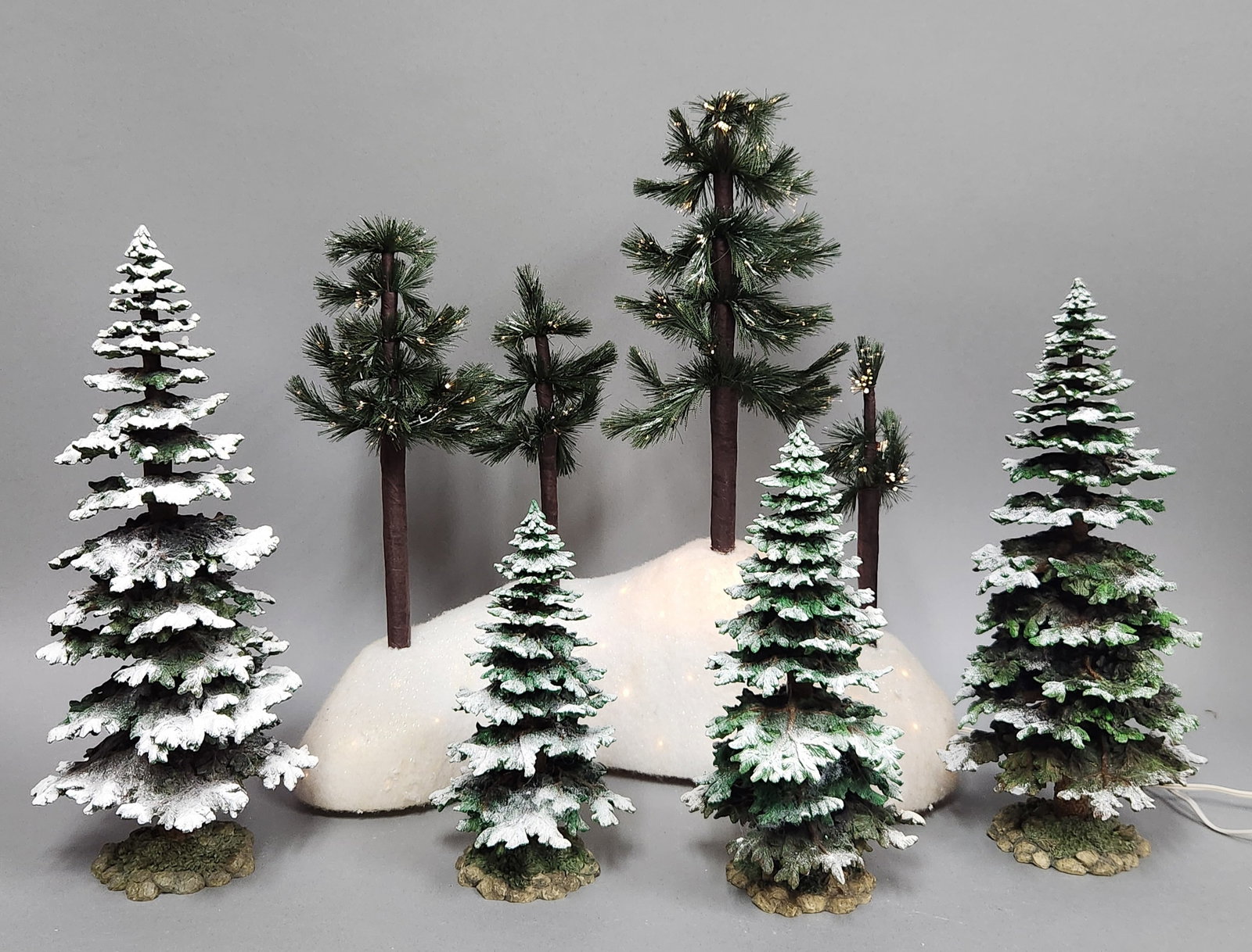 Dept 56 Illuminated & Flocked Evergreen Trees: A collection of decorative miniature trees intended for holiday village displays, including an illuminated scenic base and several freestanding elements. Tallest tree height: 16 inches. The collection