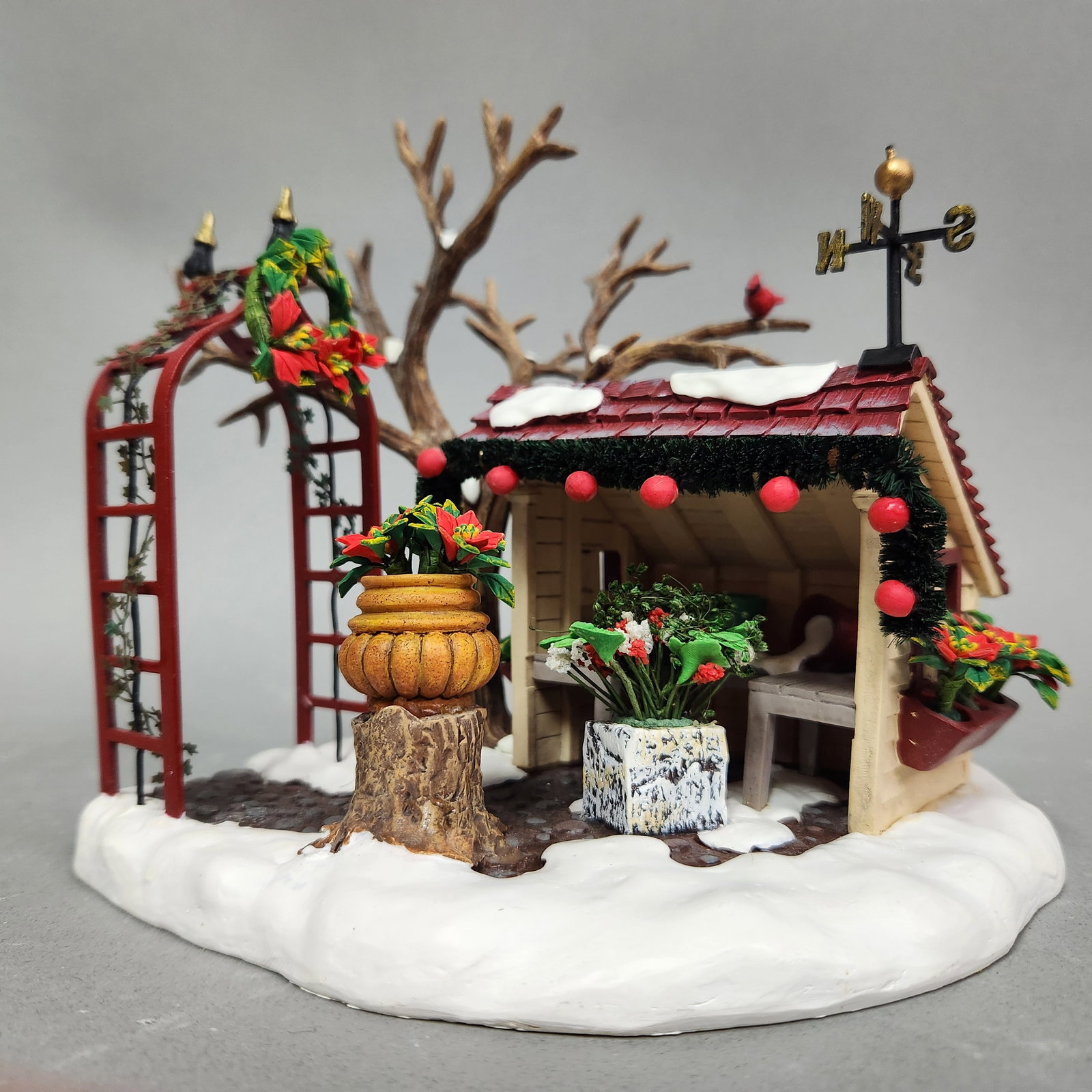 Dept 56 Winter Trimmings: A Department 56 Winter Trimmings #56.53107 village accessory featuring a decorated garden shed, red trellis, and bare tree on a snowy base measuring approximately 7 by 5 inches. Original box. Very