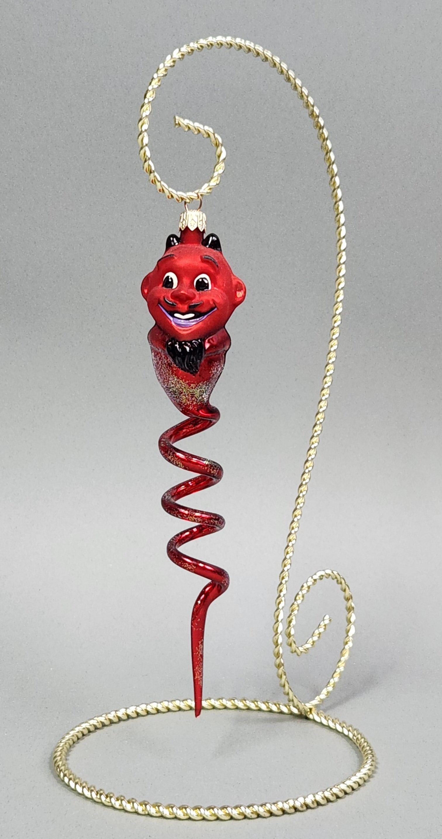 Italian Glass Devil Ornament: Stand not included. A red glass Christmas ornament depicting a stylized devil with a spiral tail and gold glitter accents, measuring approximately 8.5 inches in length and featuring a metal cap emboss