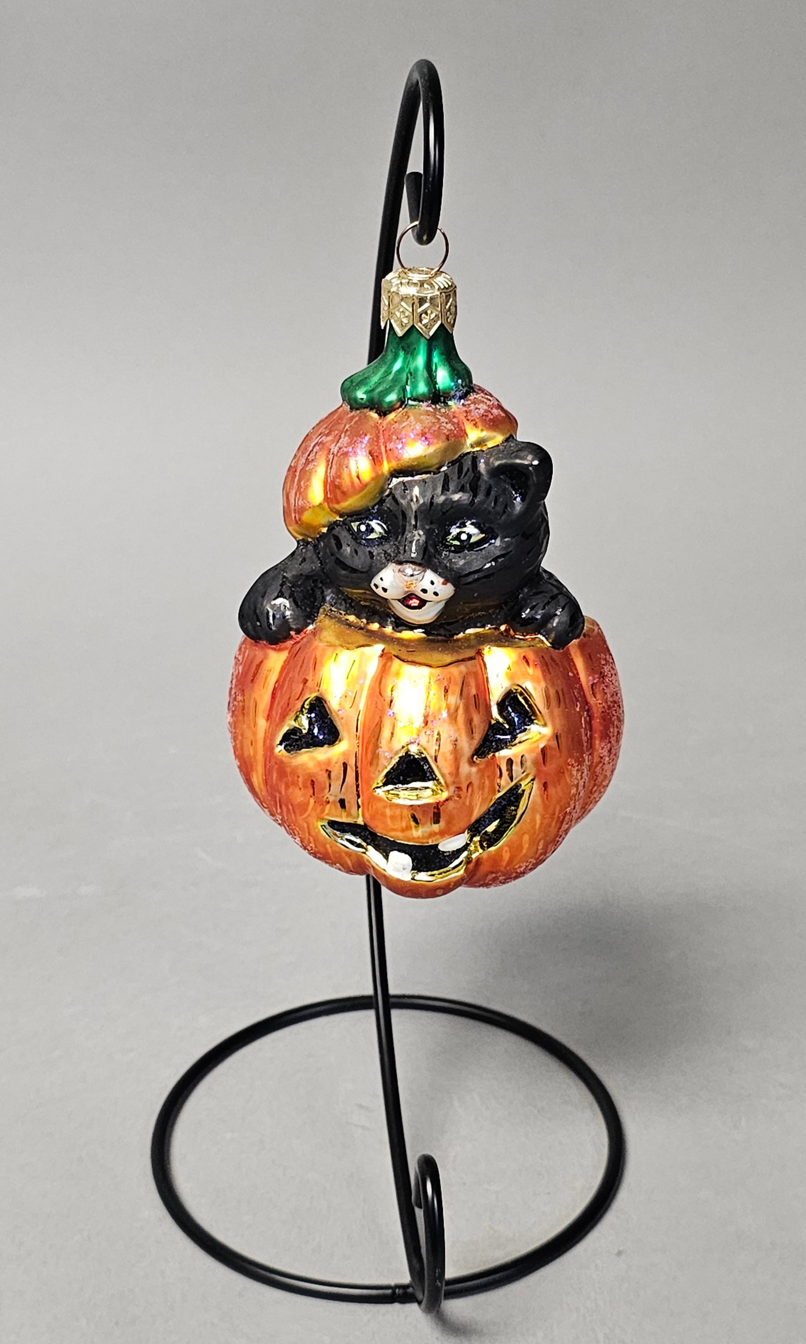 Radko Cat in Jack-O-Lantern Ornament: *STAND NOT INCLUDED*A hand-blown glass holiday ornament by Christopher Radko, specifically the Puss-Boo model from the Halloween collection. This piece features a black cat with green eyes and a