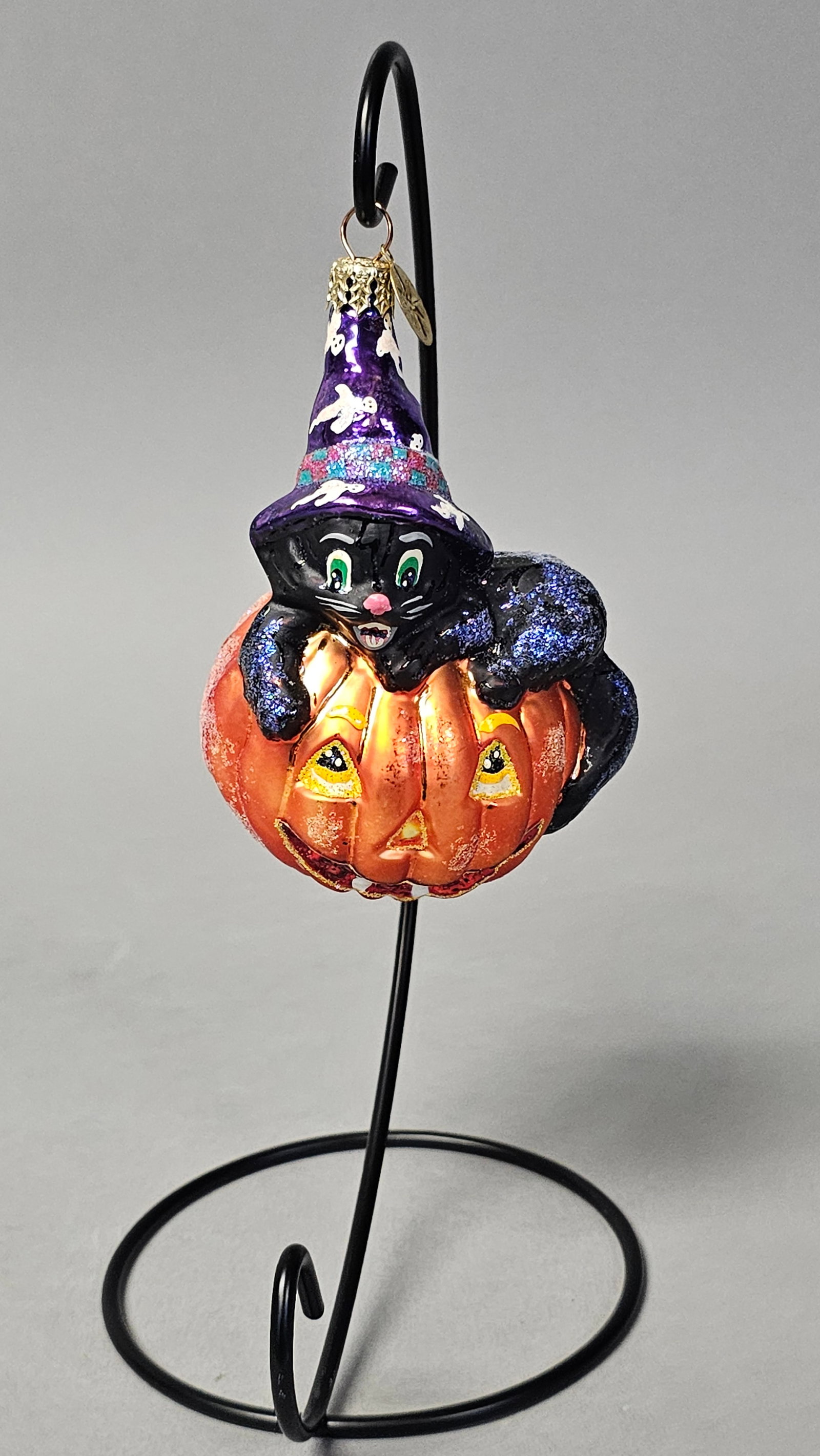 Radko Halloween Cat & Jack-o-Lantern Ornament: *STAND NOT INCLUDED* A hand-painted, mouth-blown glass Halloween ornament produced by Christopher Radko. The piece features a whimsical black cat wearing a purple witch's hat, perched atop an orange