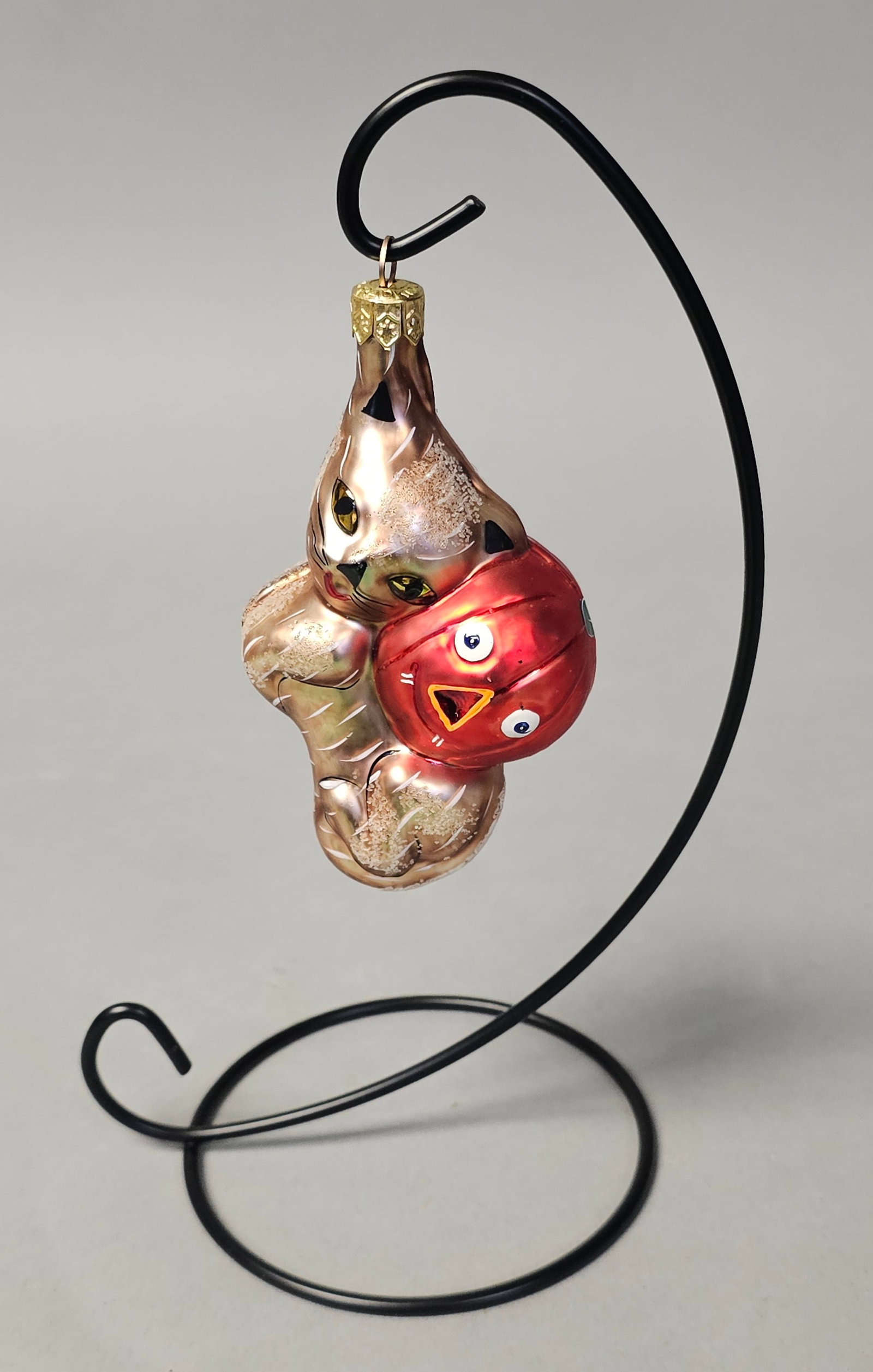 Radko Halloween Cat & Jack-O-Lantern Ornament: *STAND NOT INCLUDED* Christopher Radko mouth-blown glass holiday ornament. This figural piece depicts a tan and gold-toned cat with brown stripes, grasping a bright red-orange jack-o-lantern. The