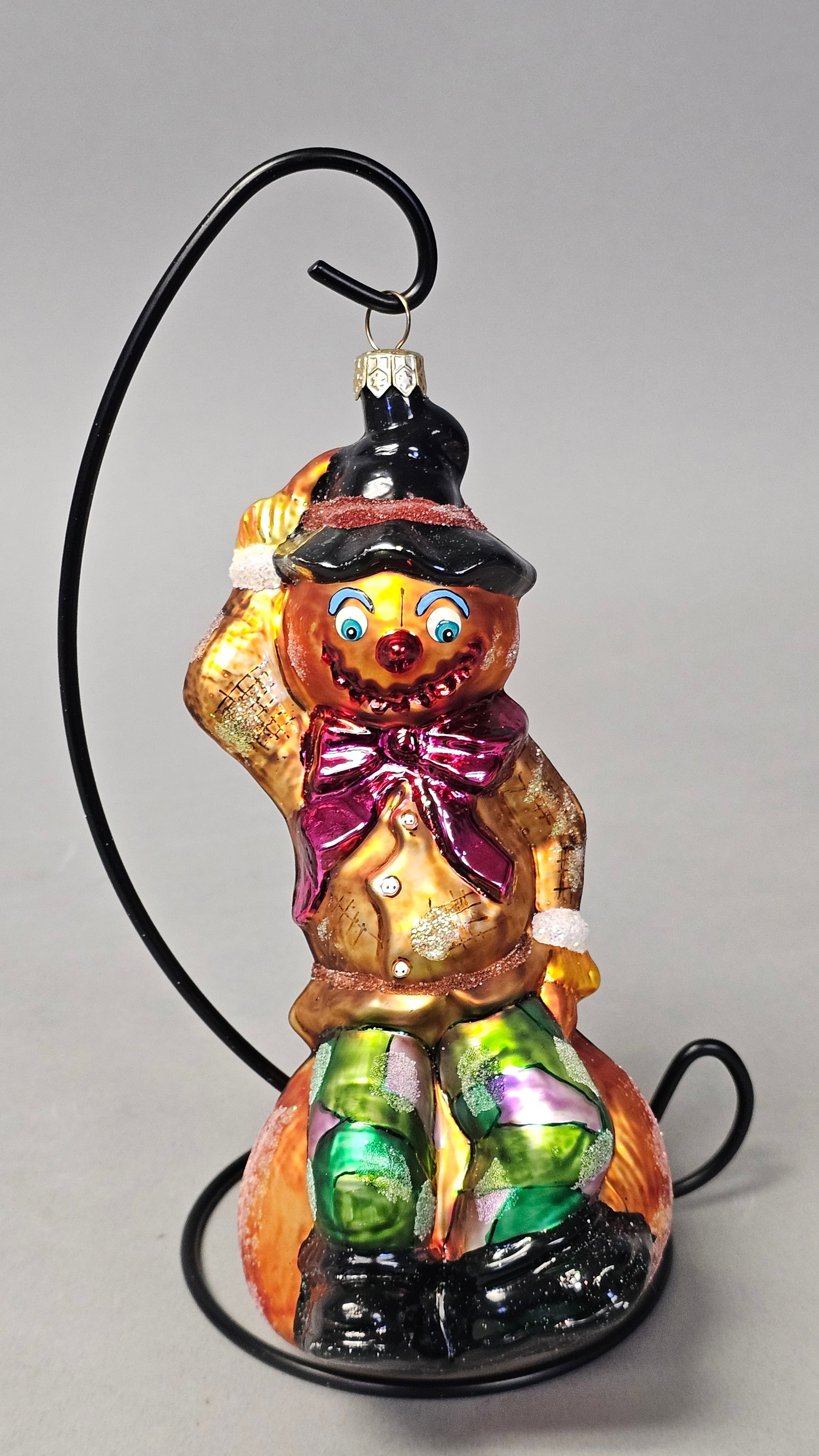 Christopher Radko Scarecrow on Pumpkin Ornament: *STAND NOT INCLUDED* A hand-blown glass holiday ornament by Christopher Radko depicting a scarecrow character seated upon a large pumpkin. The piece is finished with hand-painted and glittered embelli