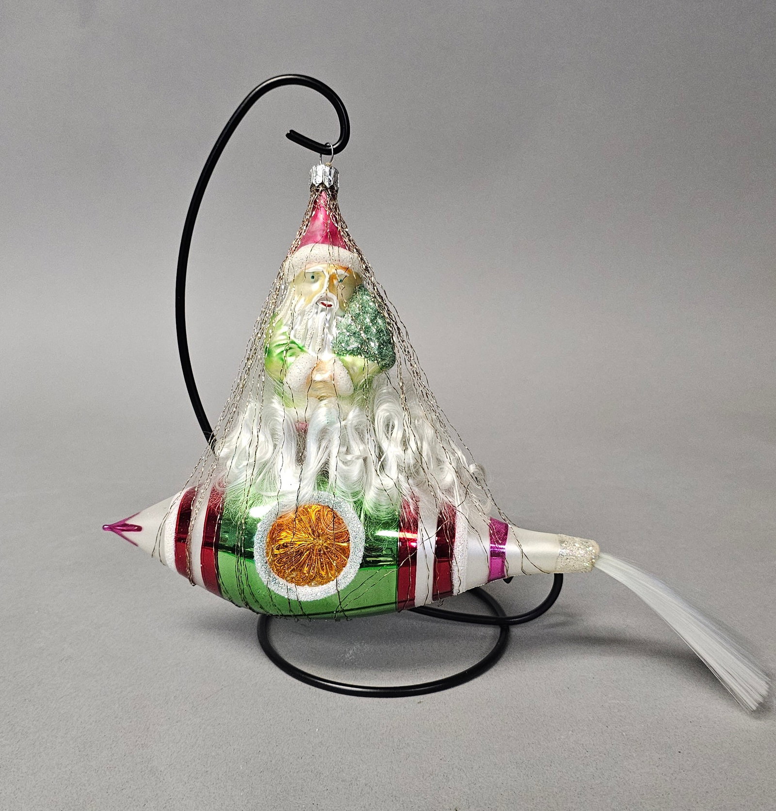 Radko Santa on Rocket Blown Glass Christmas Ornament: *STAND NOT INCLUDED* This is a large, hand-blown glass Christmas ornament produced by Christopher Radko. The ornament features a whimsical design depicting Santa Claus seated atop a rocket or dirigibl
