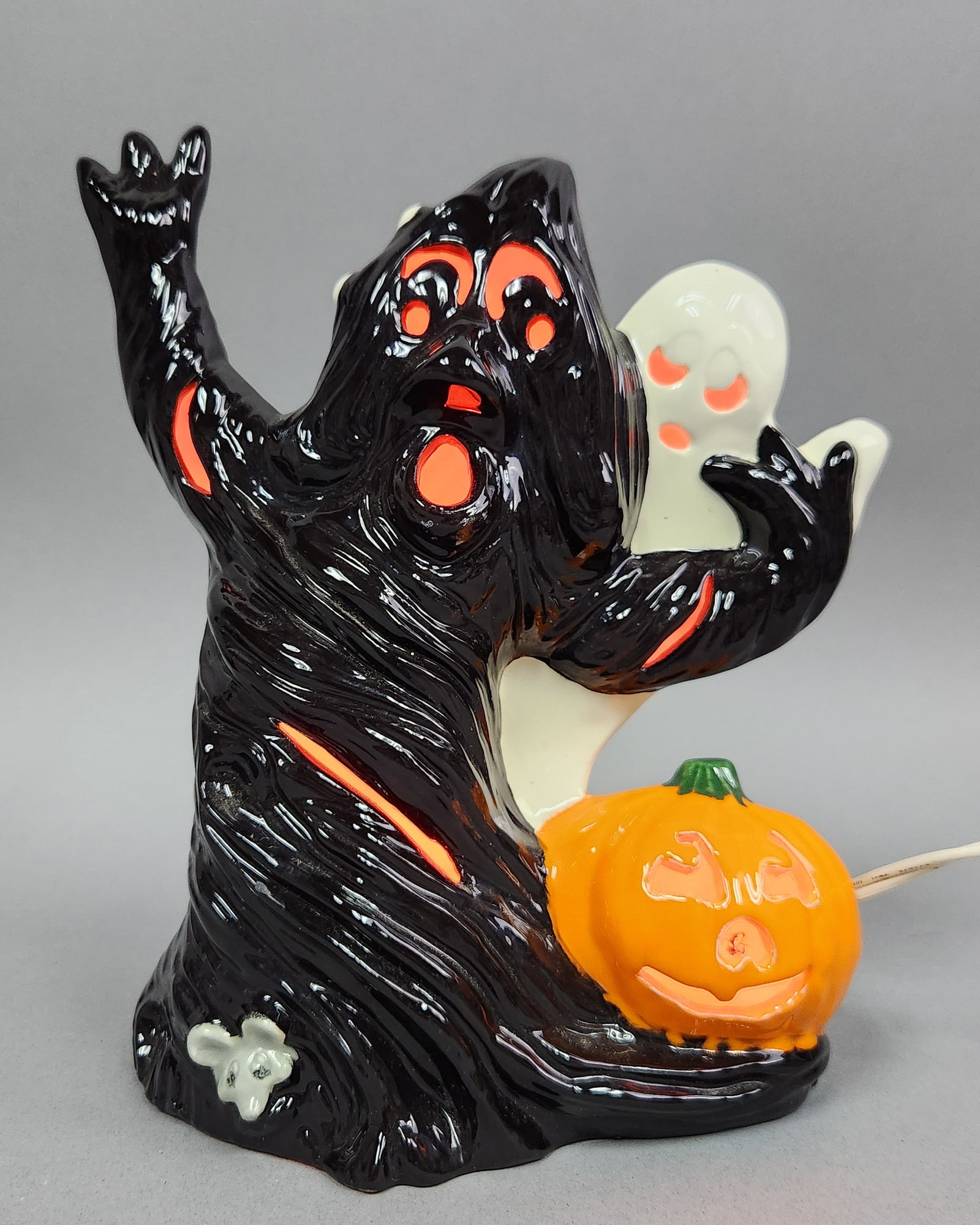 Lighted Spooky Ceramic Figurine: A single hand-painted ceramic Halloween light-up figurine featuring a large, glossy black ghost with cut-out eyes and mouth. Height: 9.5 inches Width: 8.5 inches. Used. The figurine shows minor