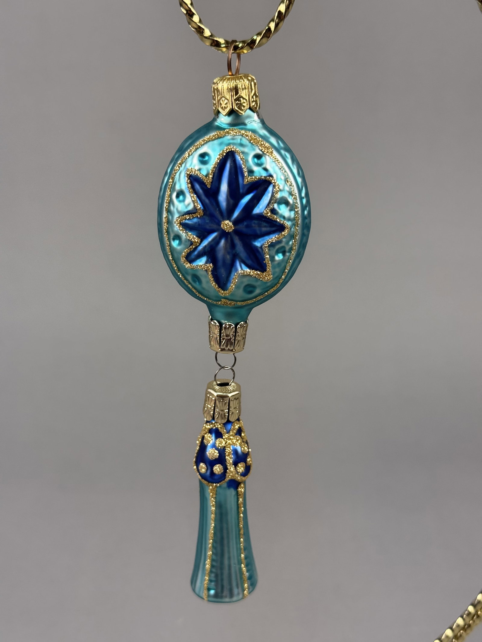 Radko Turquoise and Royal Blue Glass Star and Tassel Drop Ornament: Stand not included. A hand-blown glass holiday ornament by Christopher Radko. The ornament is finished with two decorative gold-tone metal caps, with the top cap bearing the embossed mark RADKO. Total