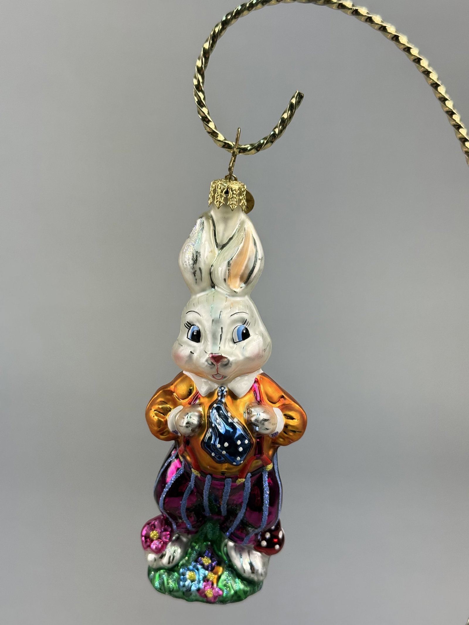 Christopher Radko Traveling Bunny Hand-Painted Blown Glass Easter Ornament: Stand not included. A hand-painted blown glass holiday ornament produced by Christopher Radko, depicting an anthropomorphic rabbit.A gold-toned metal cap is fixed to the top, and a circular gold-toned