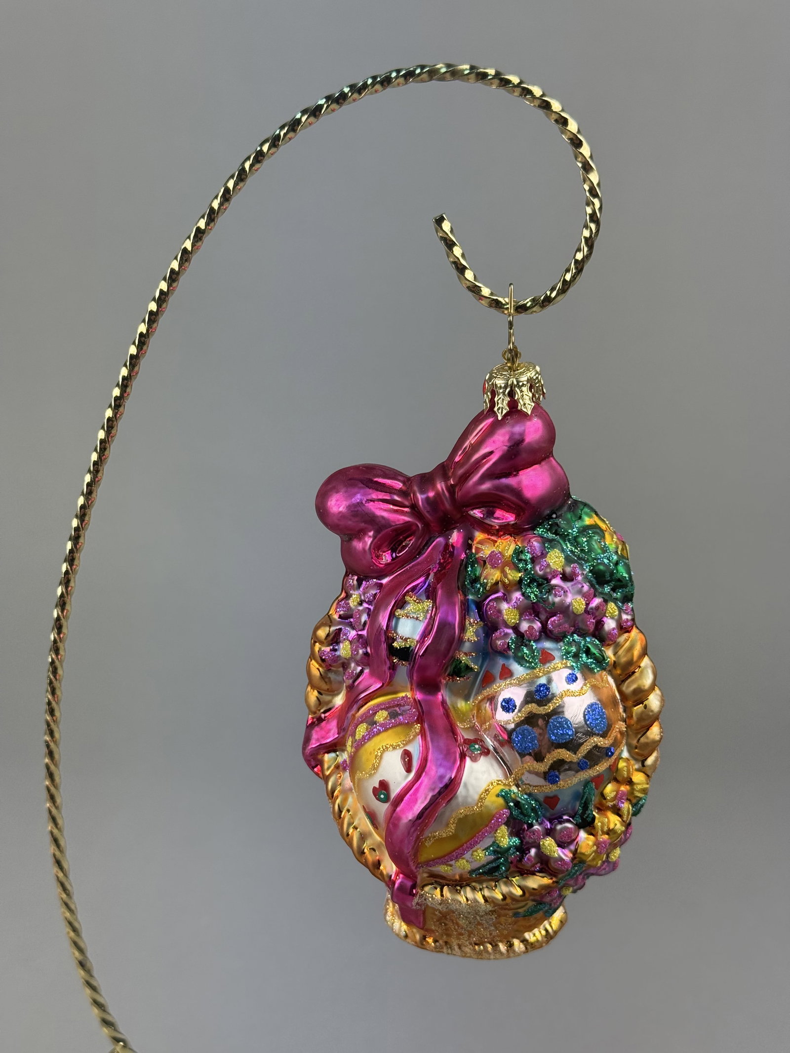 Radko Easter Bonanza Glass Basket Ornament: Stand not included. A hand-blown glass ornament designed by Christopher Radko, identified as the Easter Bonanza pattern. A gold-toned metal crown cap is fitted to the top, accompanied by the signature