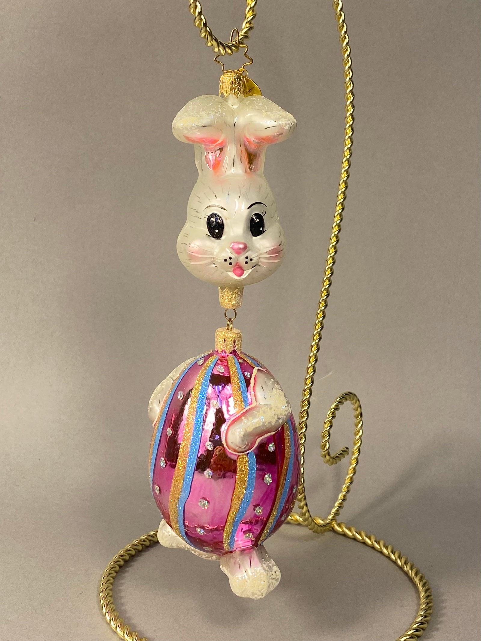 Radko Hand-Blown Glass Easter Bunny Ornament: Stand Not Included. A large two-part hand-blown glass holiday ornament by Christopher Radko with an Easter theme. The top portion depicts a stylized rabbit head in a pearlescent white finish with