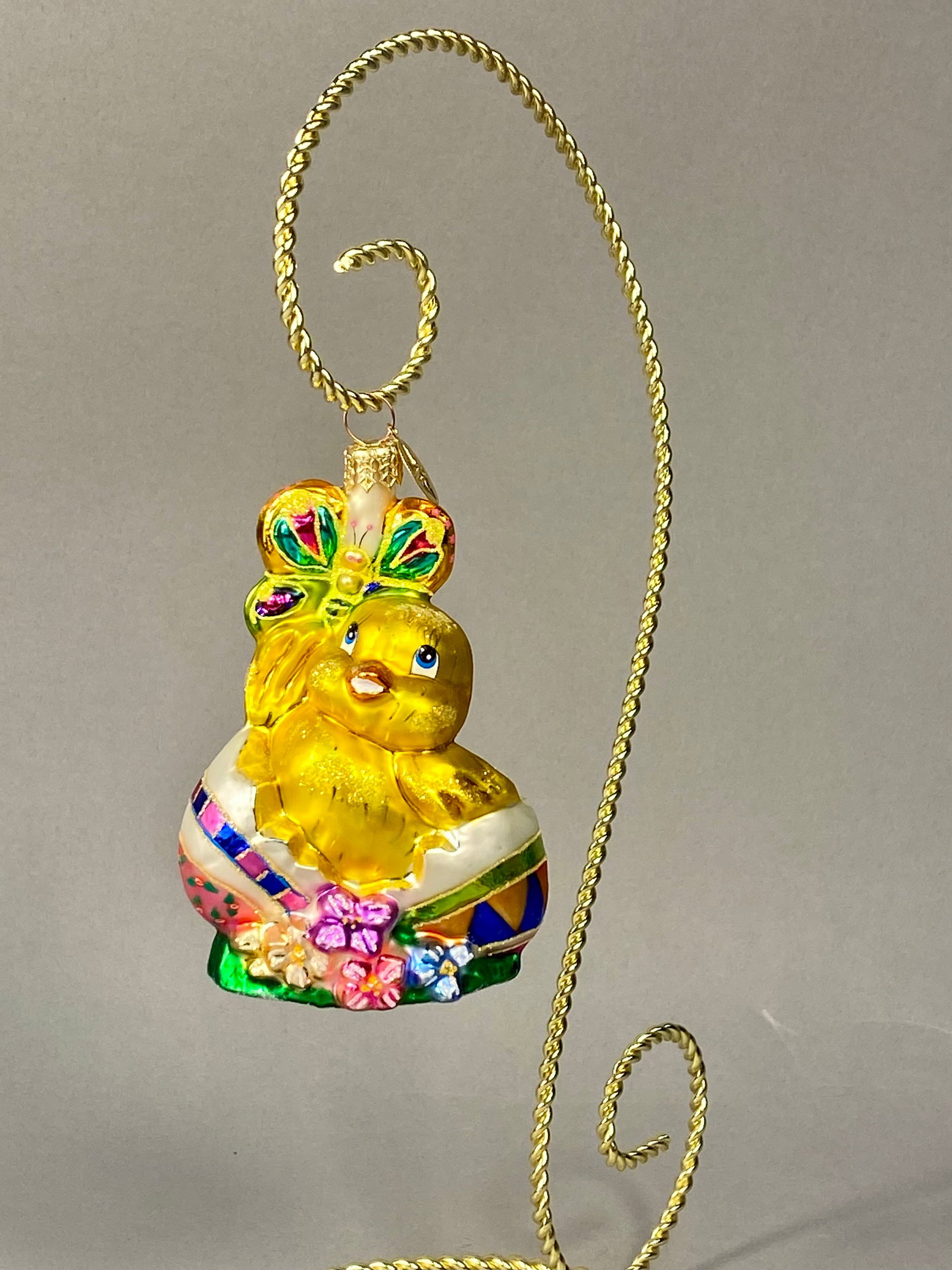 Radko Easter Chick and Egg Ornament: Stand Not Included. This hand-painted, mouth-blown glass holiday ornament by Christopher Radko, features a whimsical Easter theme. The piece depicts a bright yellow chick hatching from a decorated