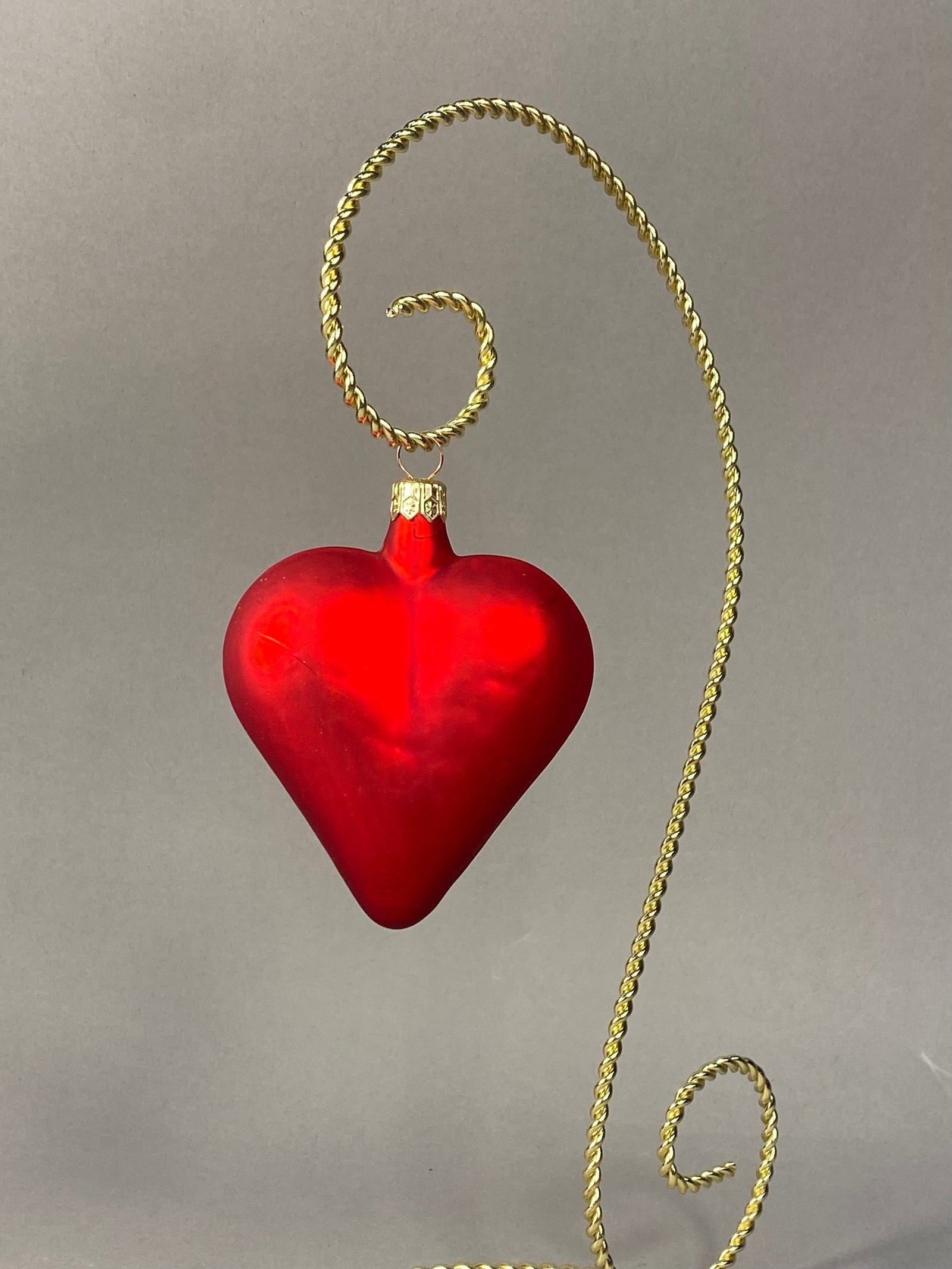 Polish Blown Glass Heart Ornament: Stand Not Included. A heart-shaped holiday ornament of blown glass construction featuring a red satin finish. The ornament is topped with a gold-toned metal cap embossed with the word POLAND and a